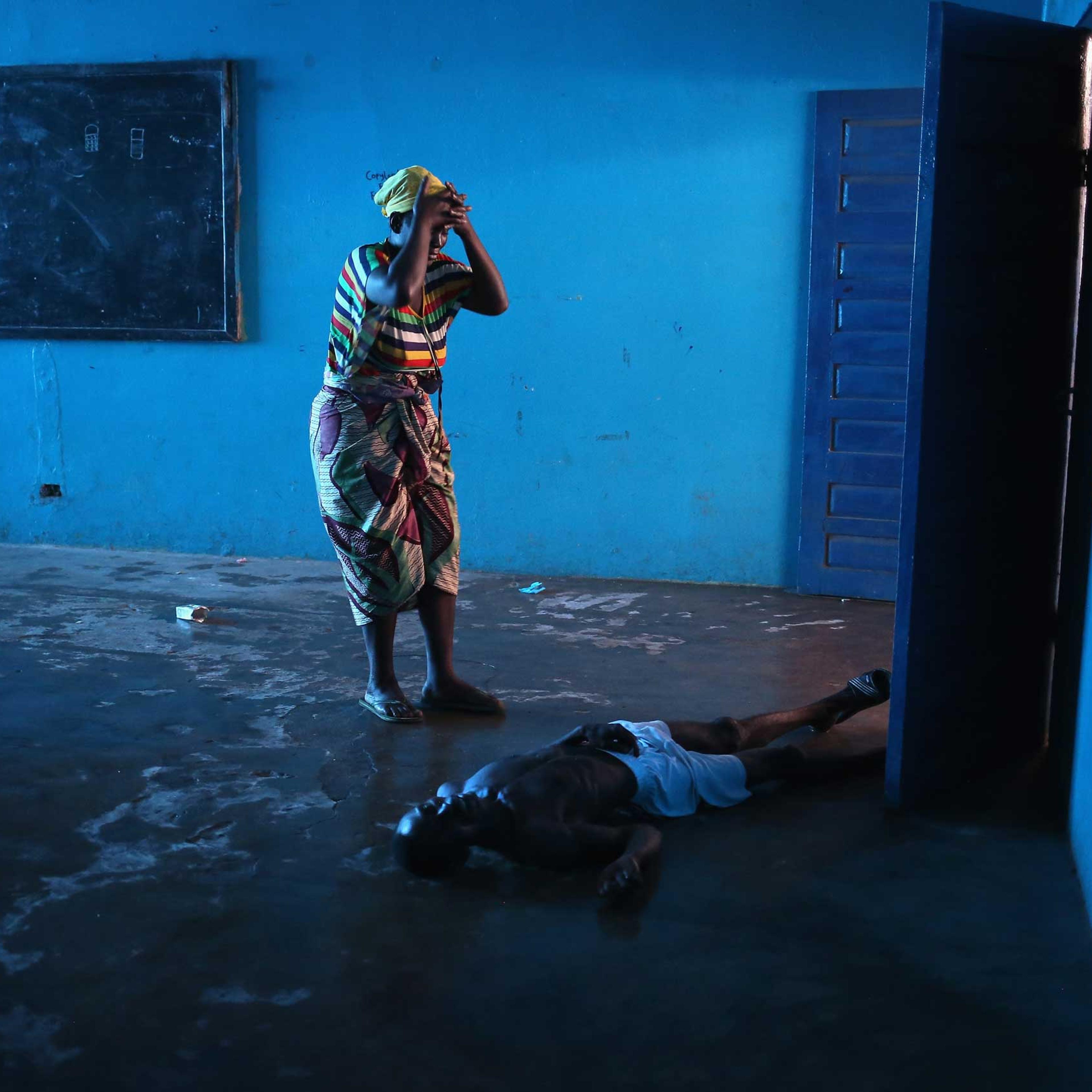 Umu Fambulle stands over her husband Ibrahim after he staggered and fell, knocking him unconscious in an Ebola ward on Aug. 15, 2014 in Monrovia, Liberia.