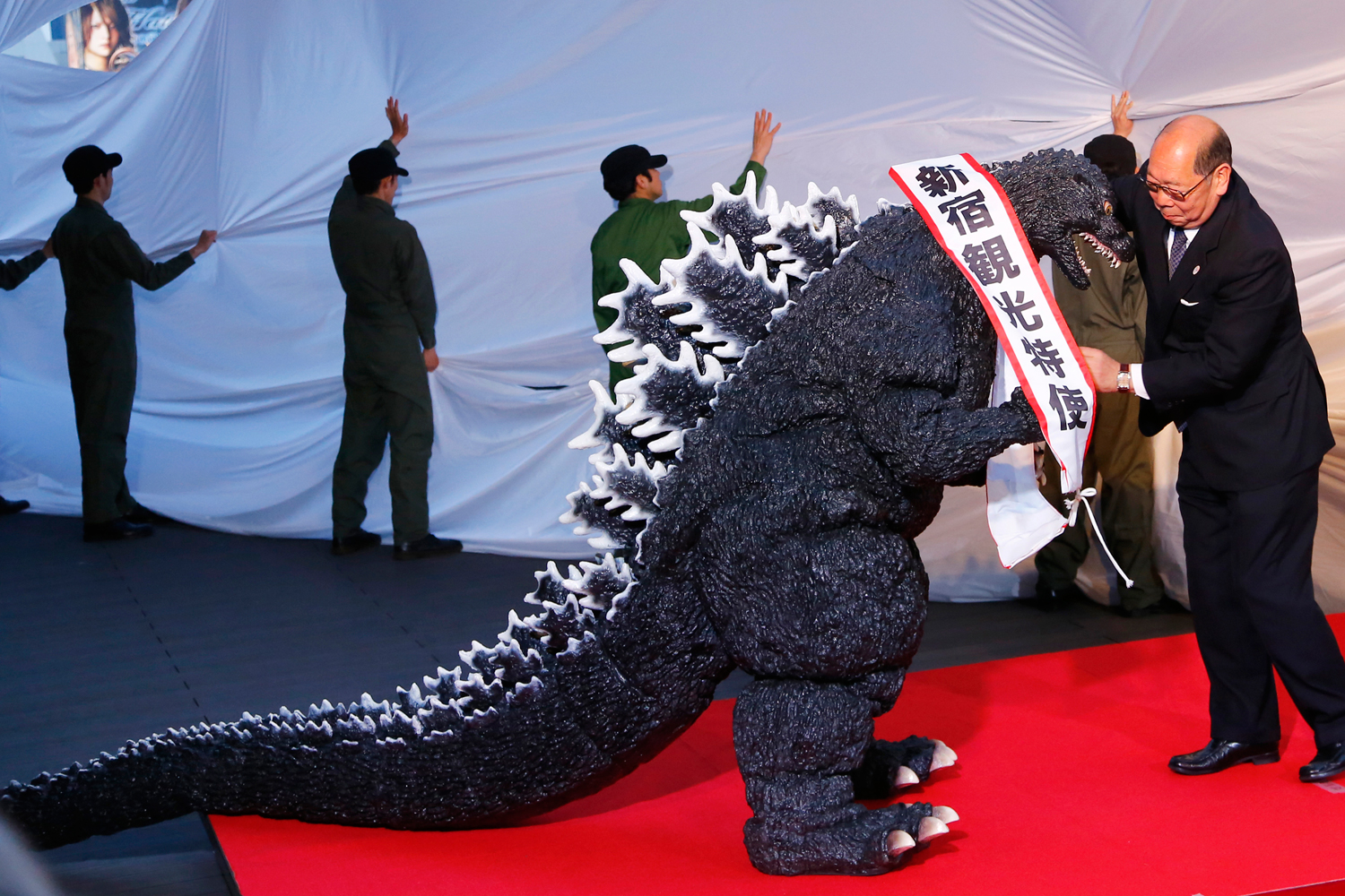 Godzilla gets a sash of "Shinjuku-ward tourism ambassador" from the Kabuki-cho Shopping Area Promotion Association Chief Director Mototsugu Katagiri of Tokyo's Shinjuku-ward during its awards ceremony in Tokyo, April 9, 2015.