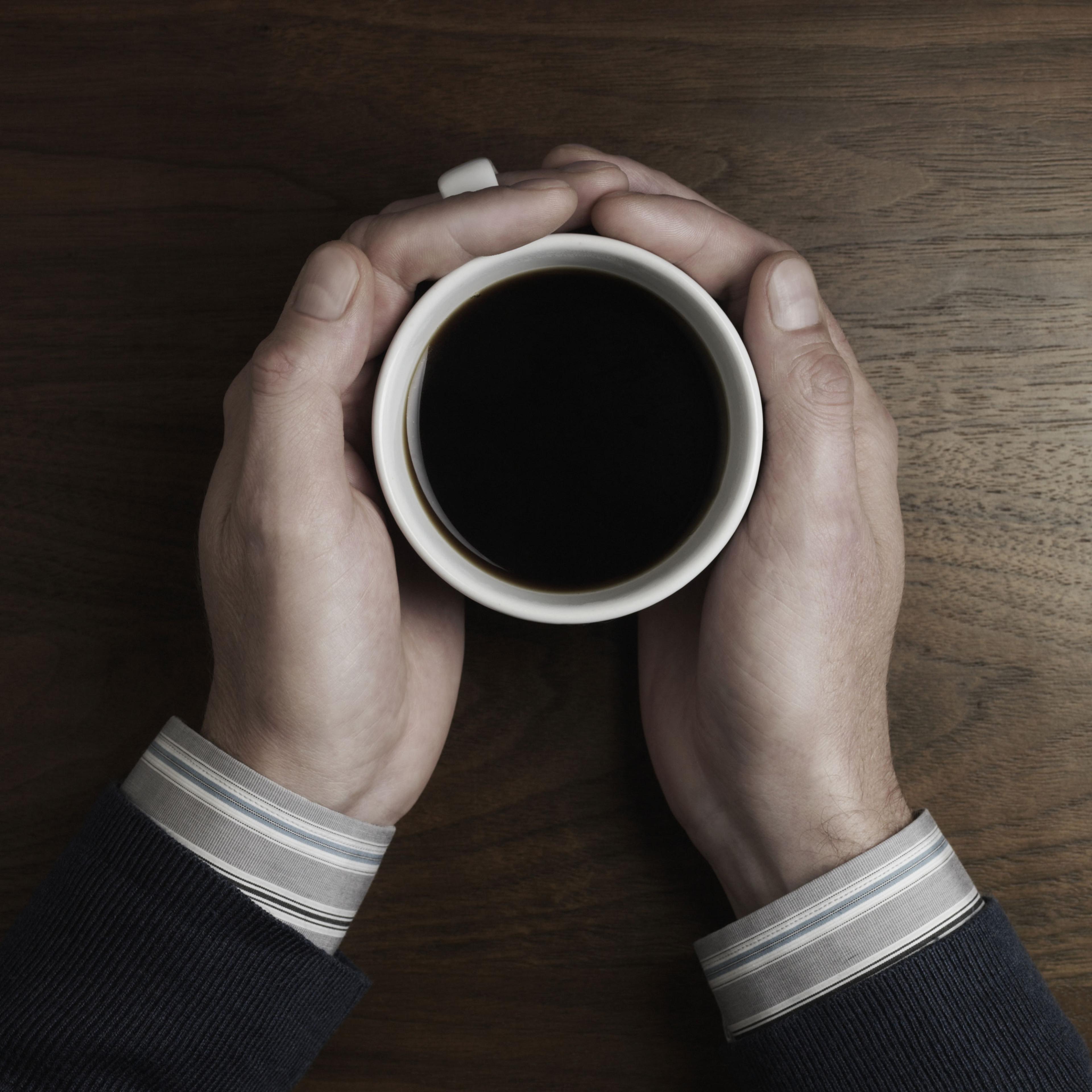 Man on desk holding cup of coffee, close up
