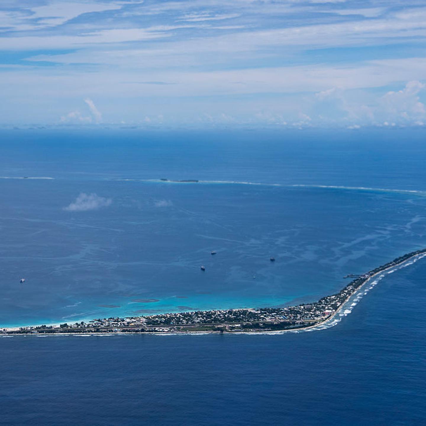 Funafuti, Tuvalu is seen from an airplane. The island is narrow and surrounded by azure sea.