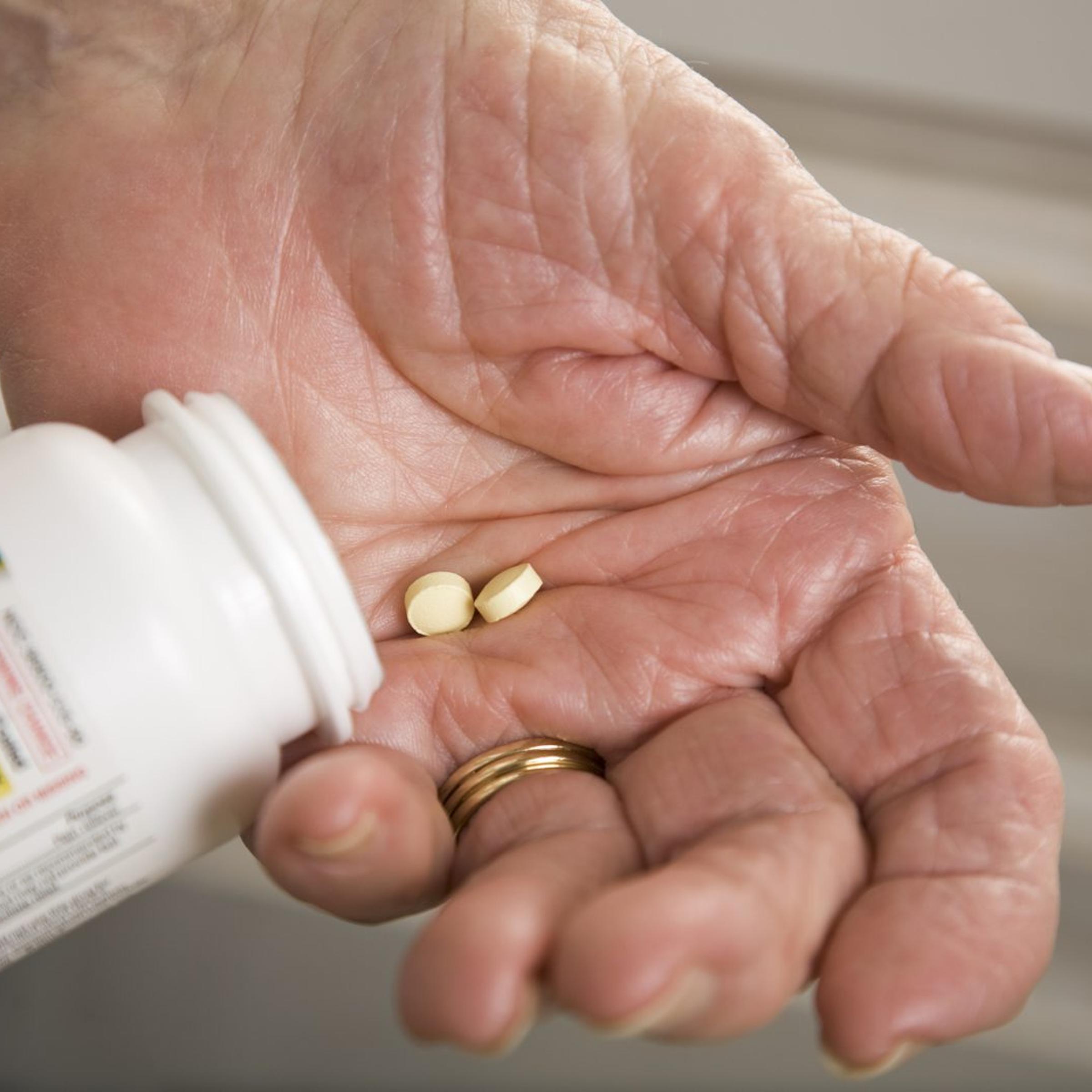 senior woman with distorted arthritis hand taking aspirin pills