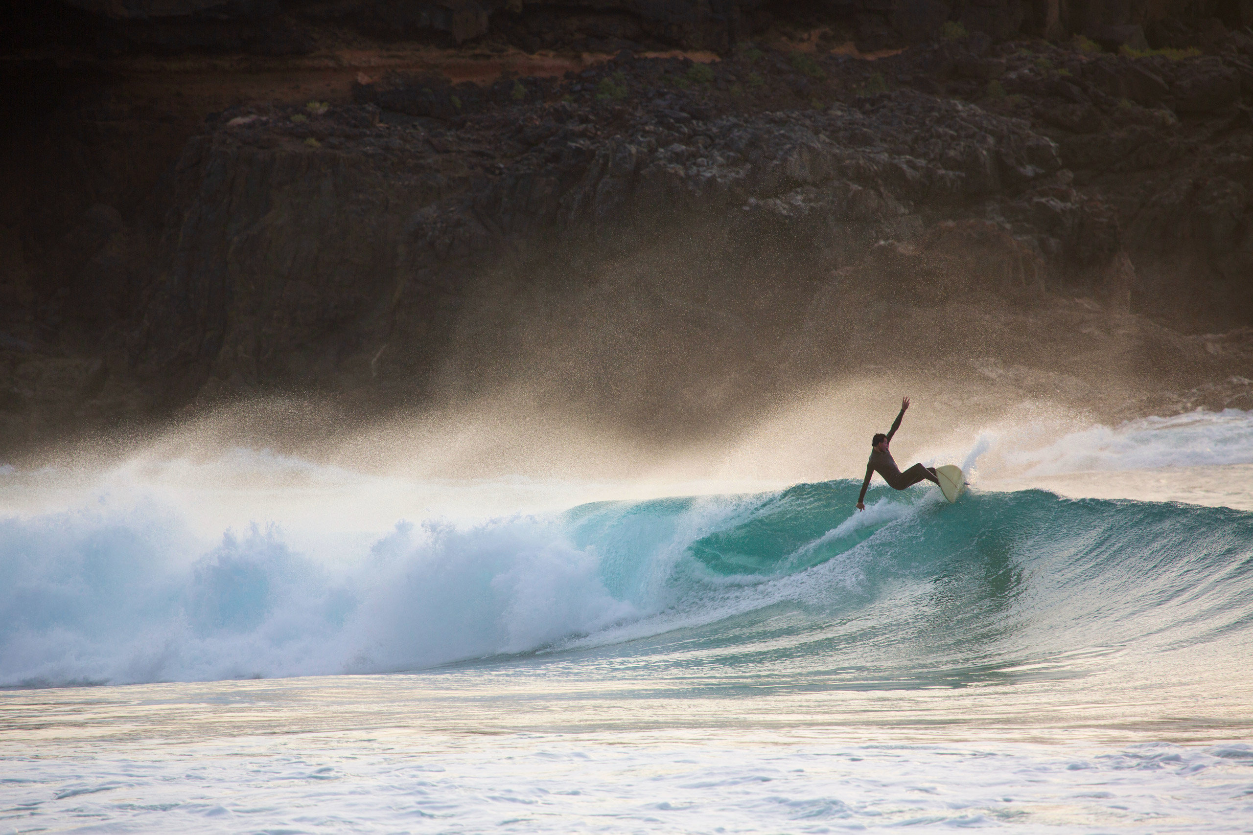 Silhouetted young man surfing wave at sunset, Fuerteventura, Spain
