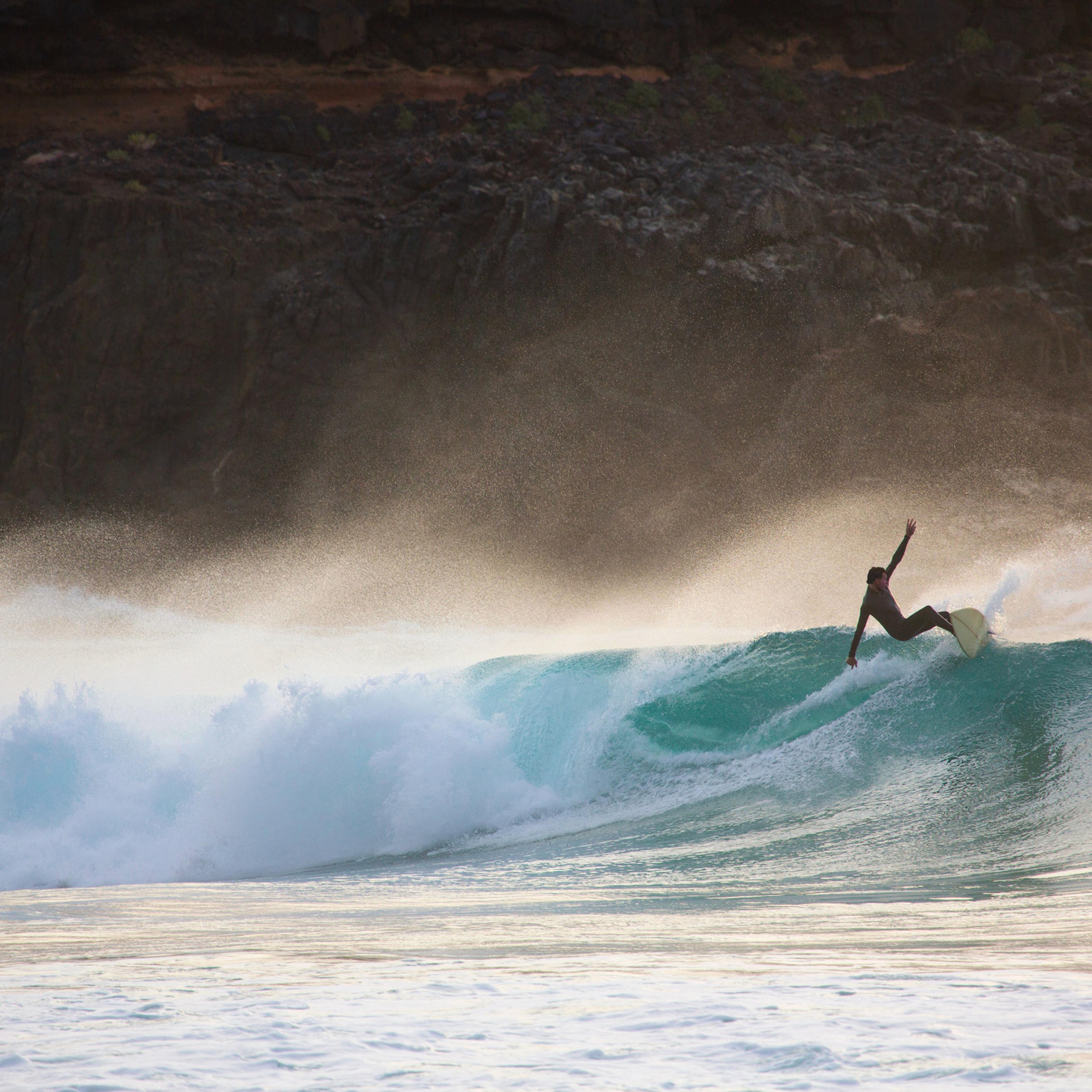 Silhouetted young man surfing wave at sunset, Fuerteventura, Spain