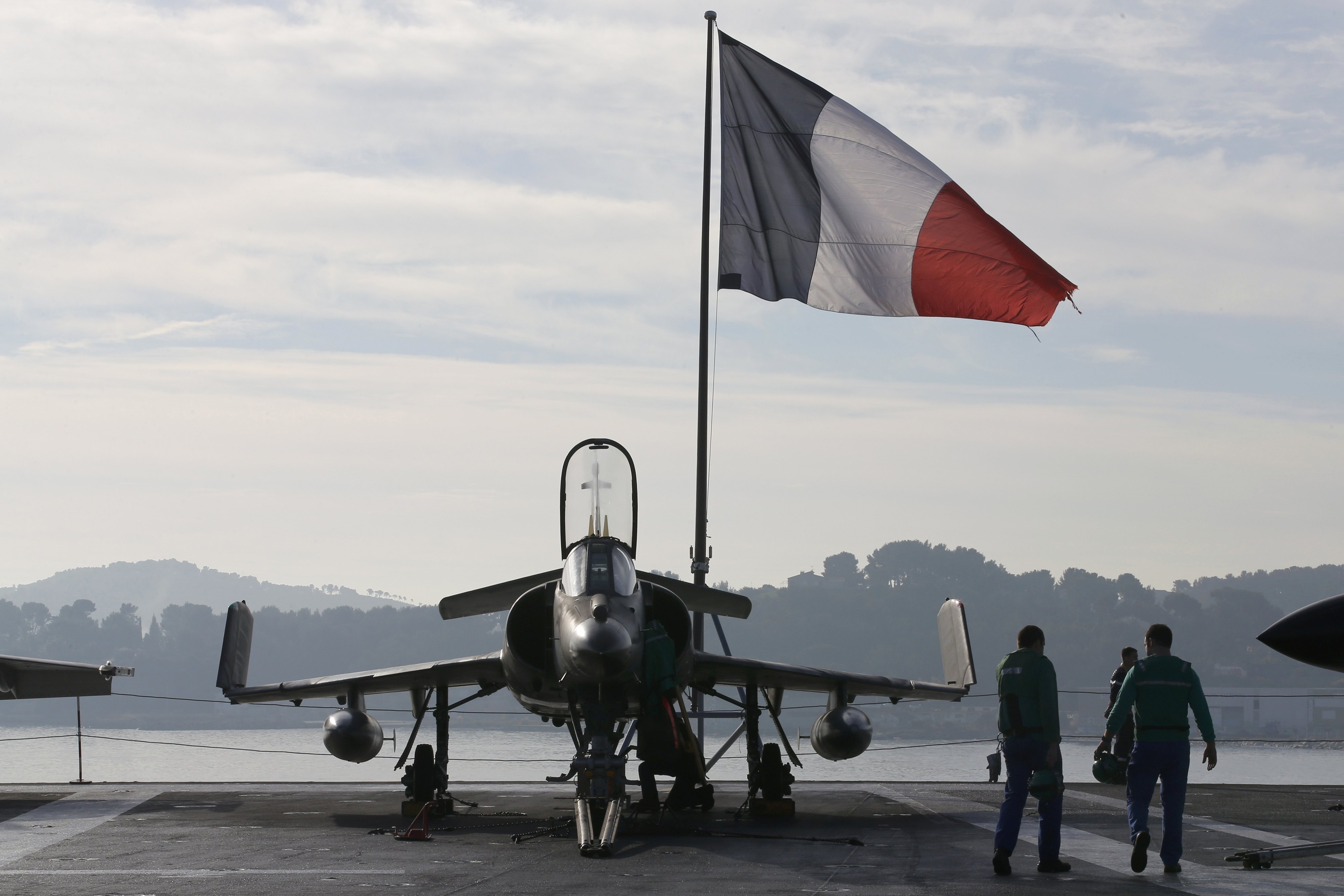 Flight deck crew work around a Super Etendard fighter jet as a French flag flies aboard the French nuclear-powered aircraft carrier Charles de Gaulle before its departure from the naval base of Toulon