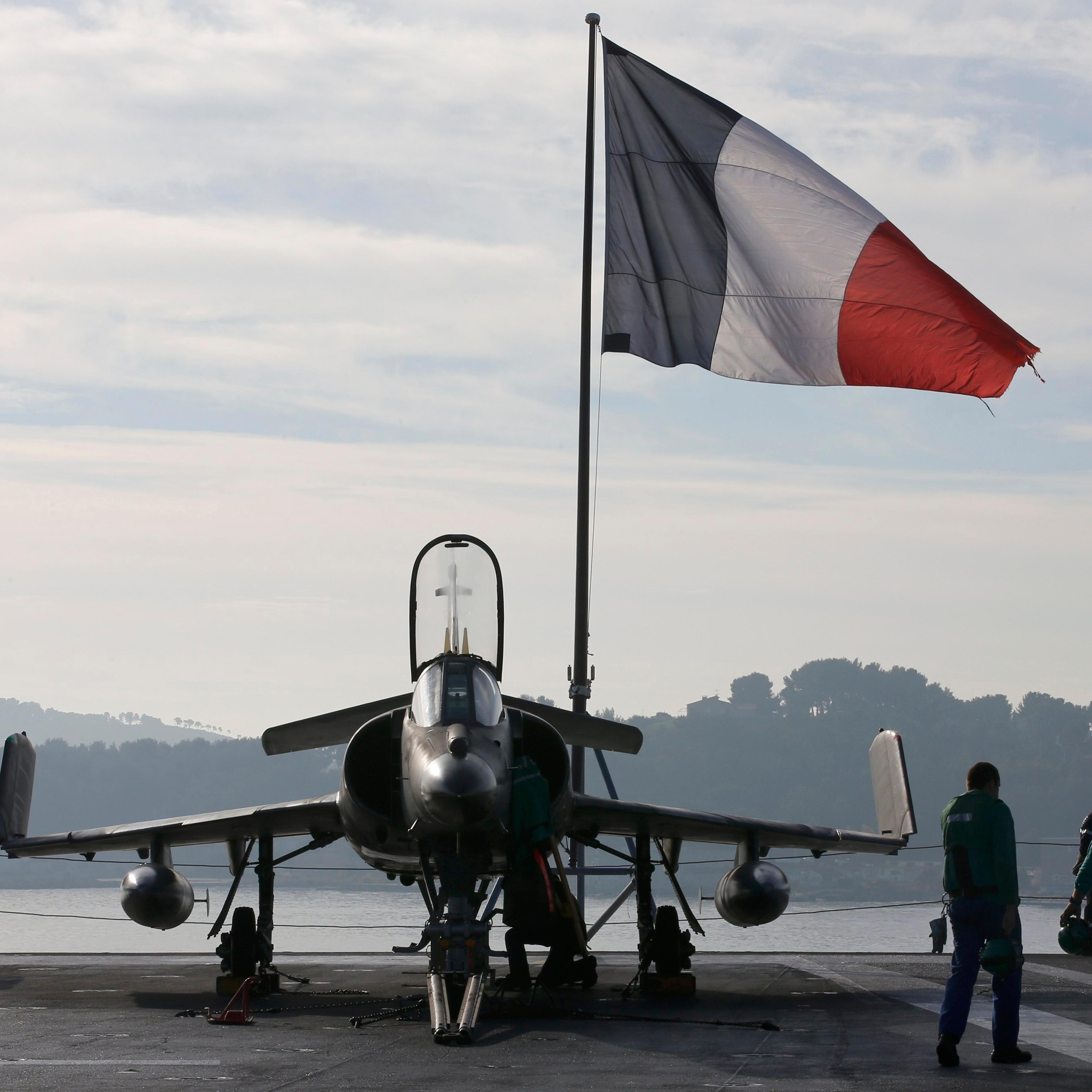 Flight deck crew work around a Super Etendard fighter jet as a French flag flies aboard the French nuclear-powered aircraft carrier Charles de Gaulle before its departure from the naval base of Toulon