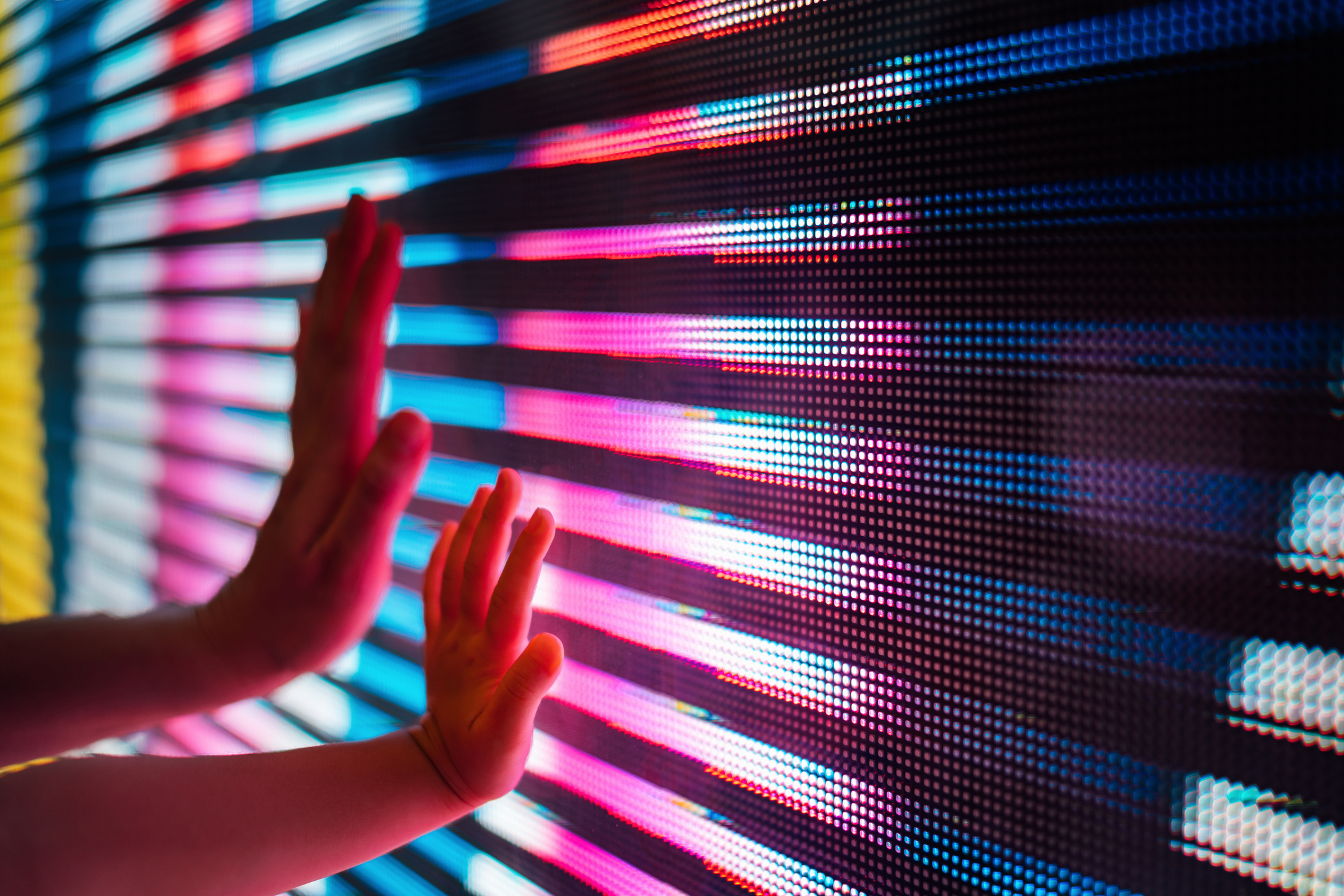 Close up of a mother and kid's hand touching illuminated and multi-coloured LED display screen, connecting to the future