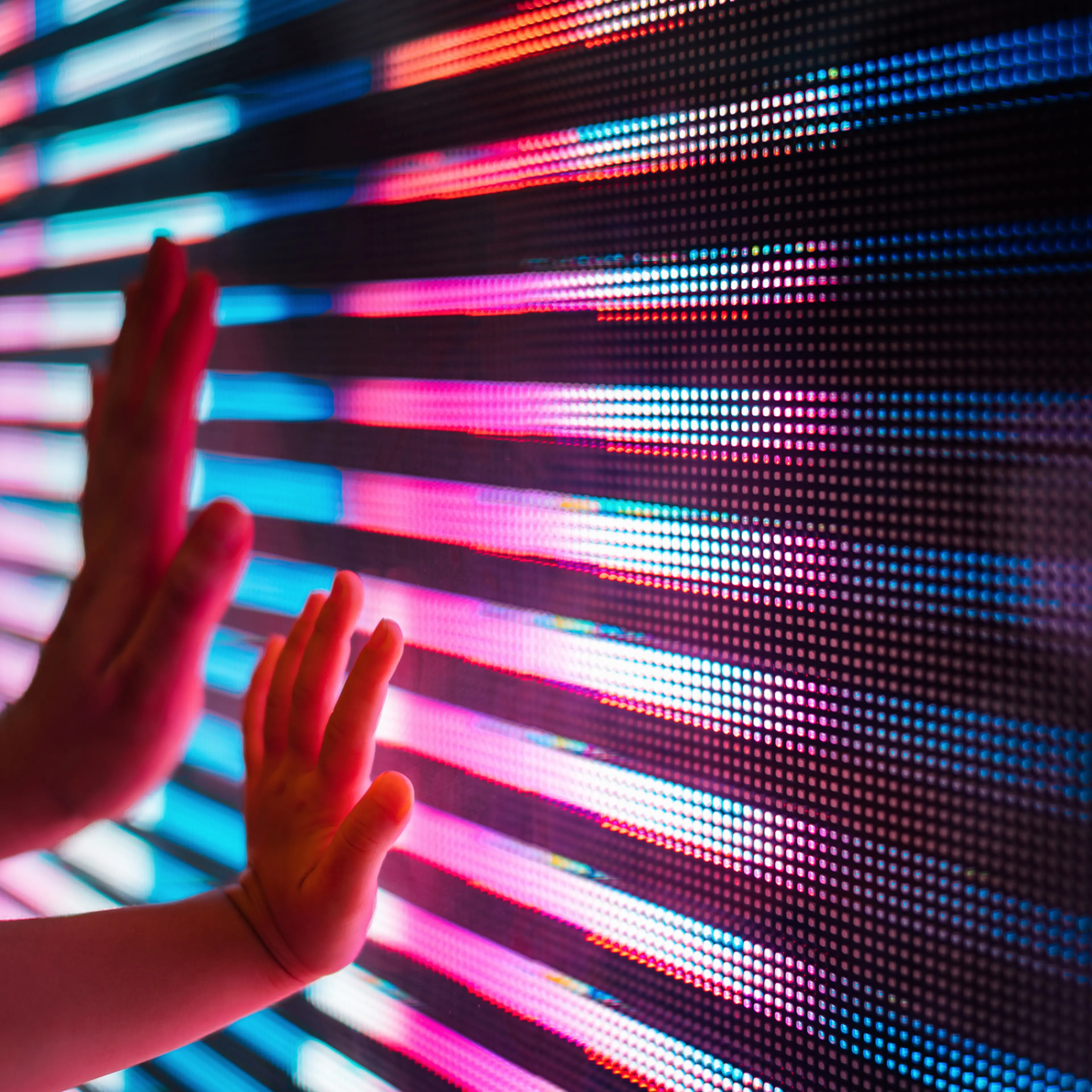 Close up of a mother and kid's hand touching illuminated and multi-coloured LED display screen, connecting to the future