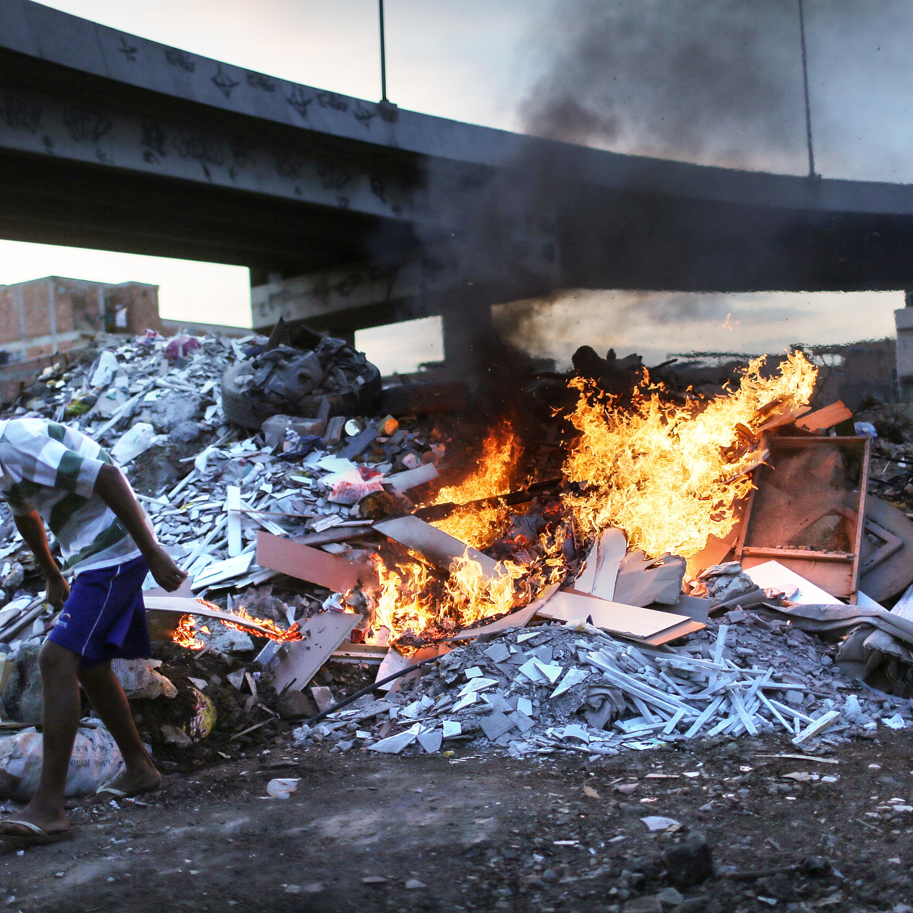 Trash is burned in an area where garbage is dumped near the main highway linking Rio's international airport to the city in the Mare favela community complex in Rio de Janeiro on July 18, 2016.