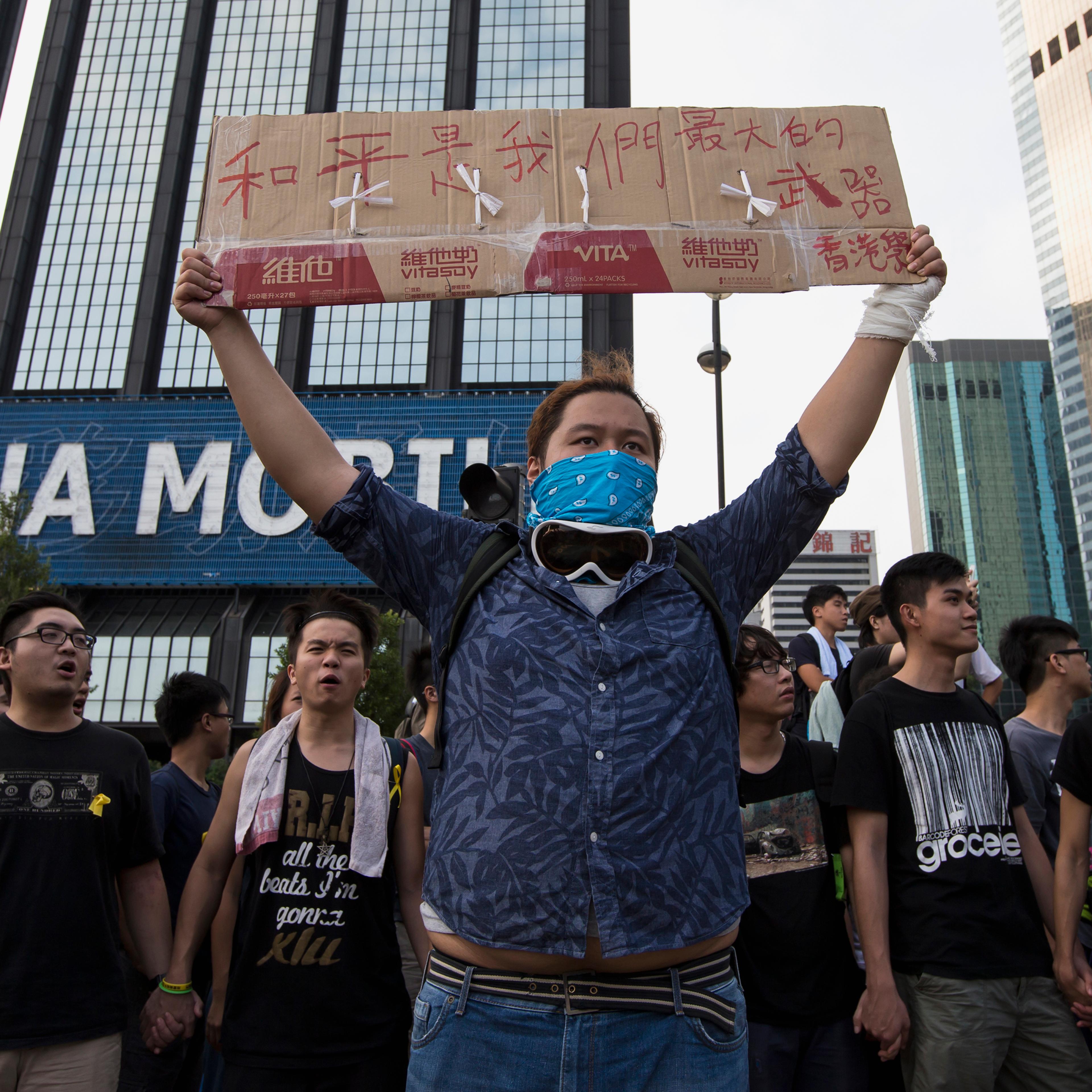 A protester holds up a placard which reads "Peace is our greatest weapon", outside the venue of the official flag-raising ceremony for celebrations of China's National Day, in Hong Kong