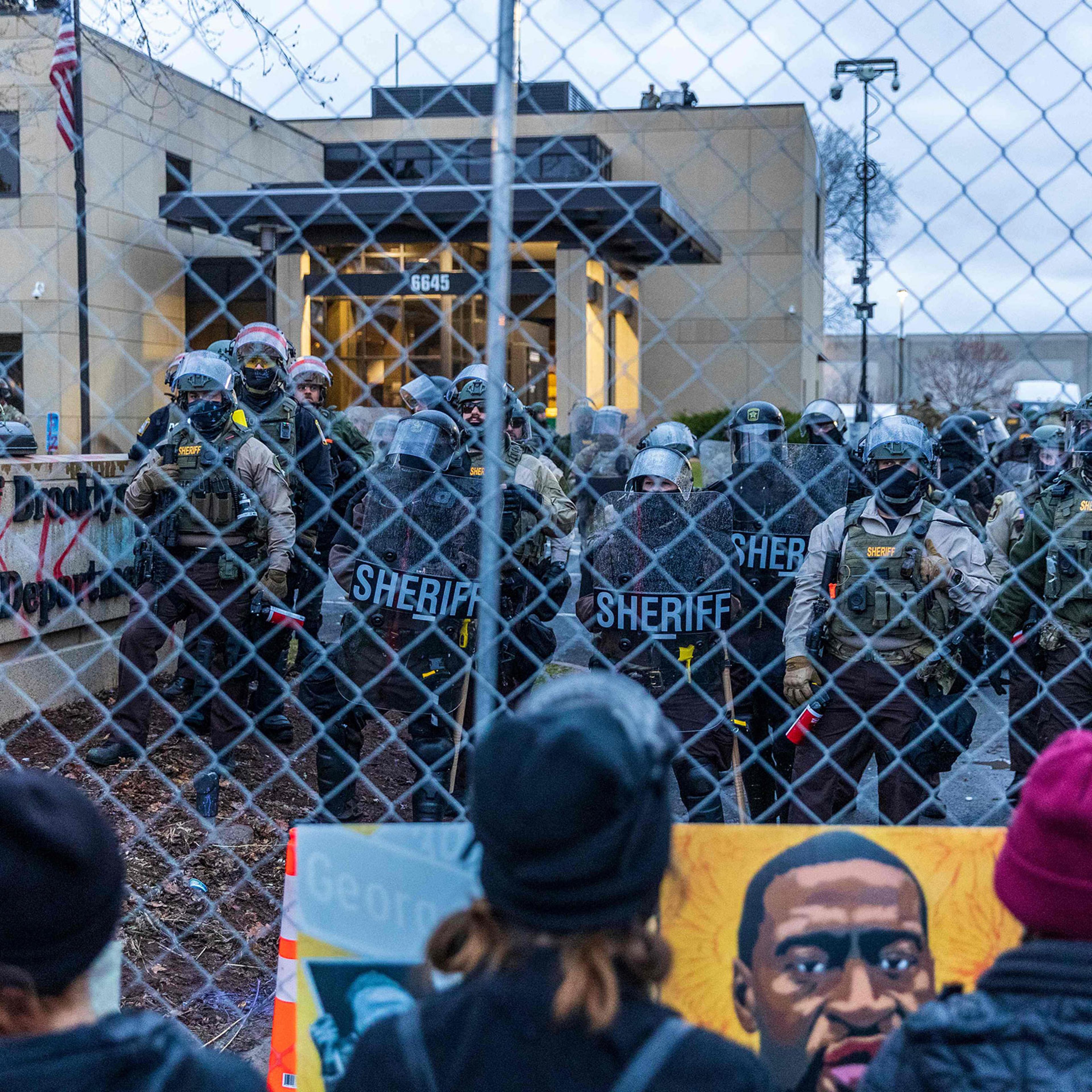 Sheriff officers stand guard outside the Brooklyn Center police station as demonstrators stand on the other side of the chain-link fence protesting the death of Daunte Wright who was shot and killed by a police officer in Brooklyn Center, Minn. on April