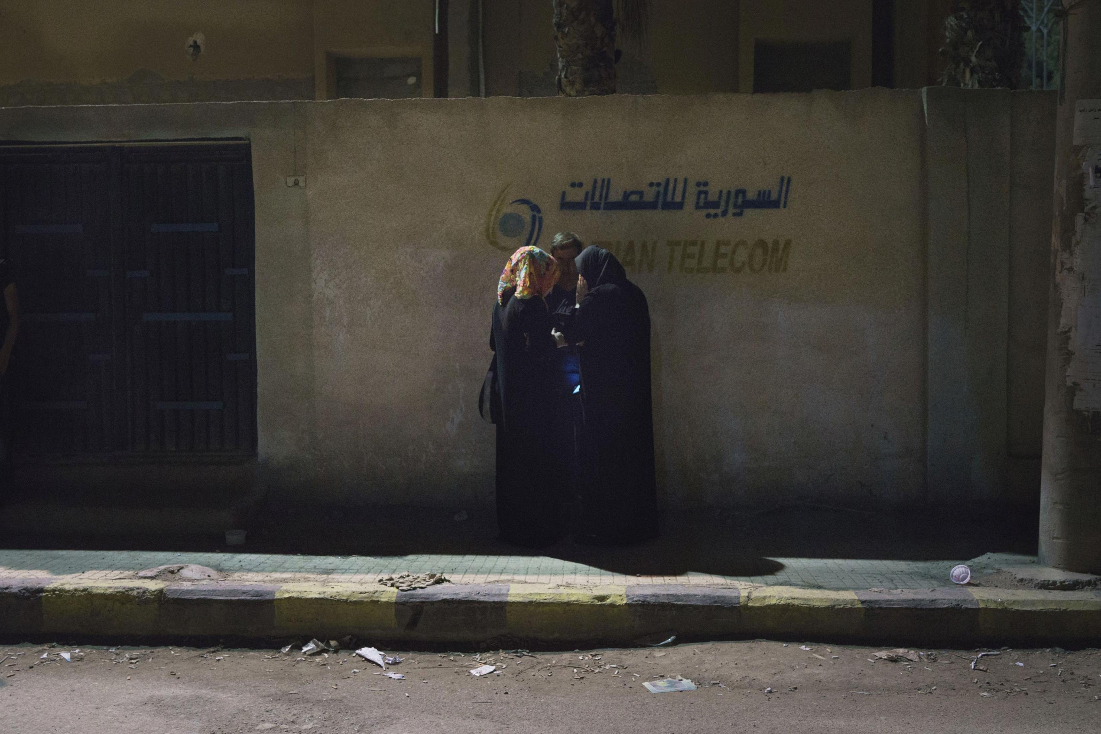 Residents of Deir-ez Zor huddle while trying to get a cell phone signal. Since the ISIS blockade of the city, electricity has been cut, making communication with the outside world difficult. Some cell towers, which are also used to provide internet service, now operate only three days a week, June 4, 2015.