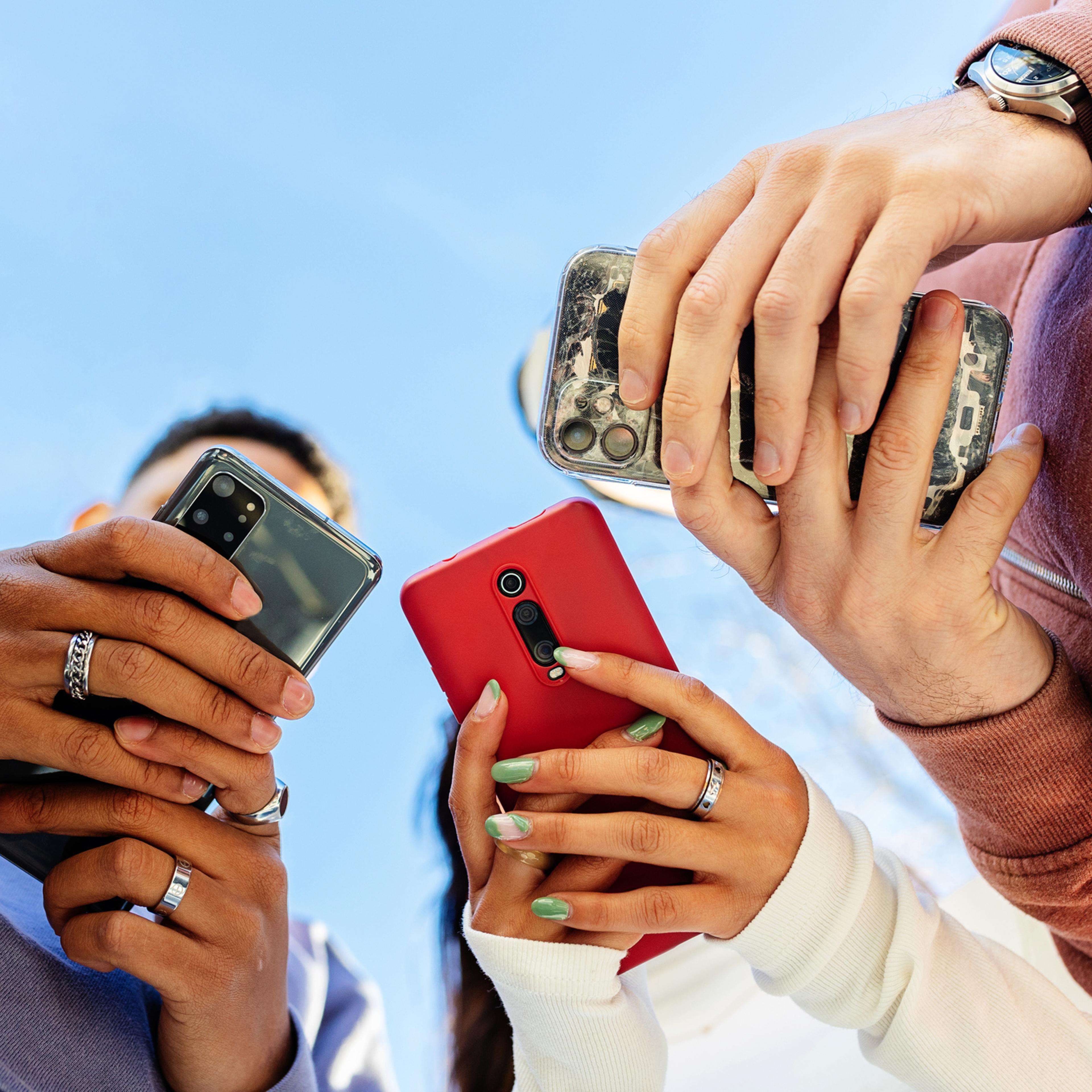 Low angle view of three young people using mobile phones outdoors