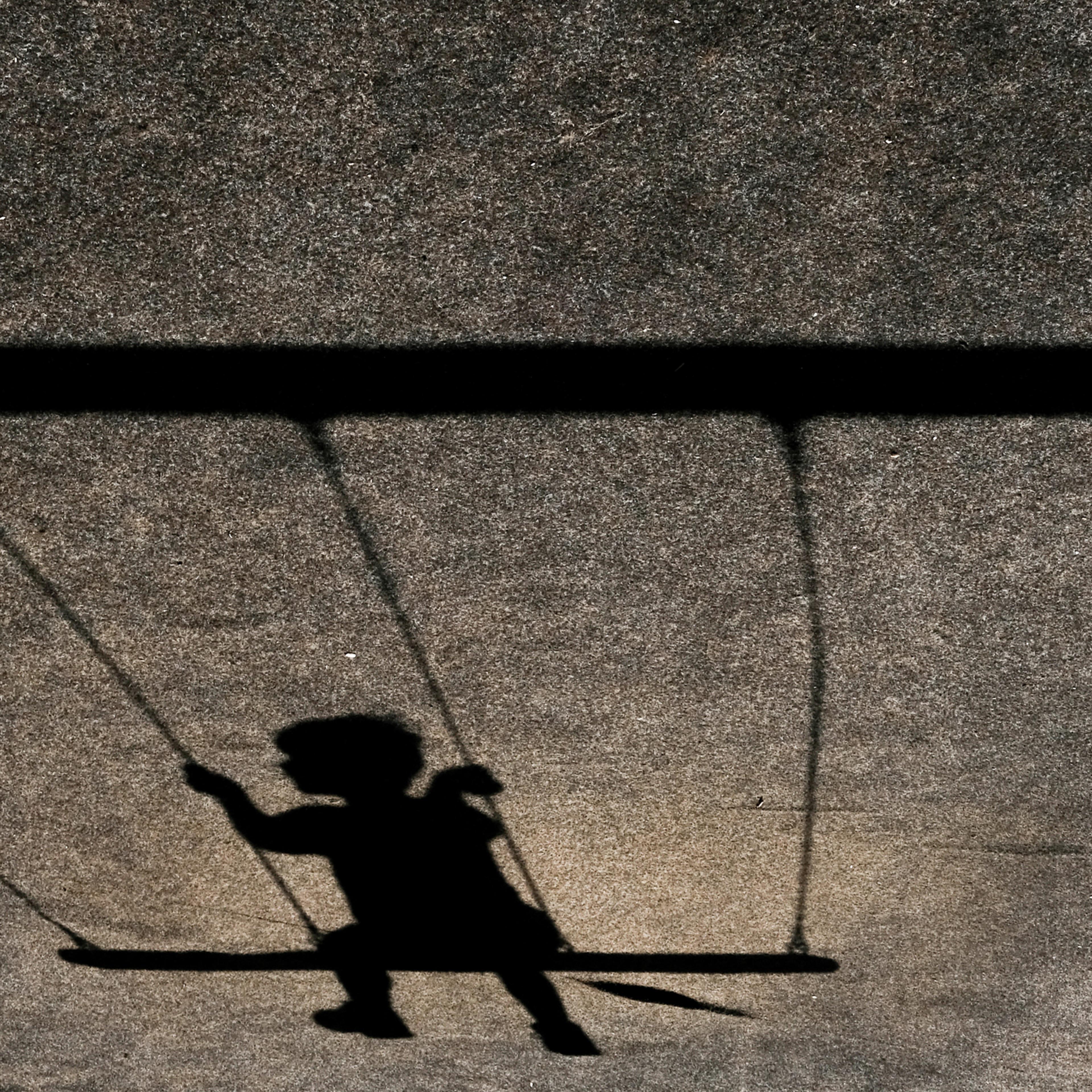 Horizontal shot of the shadow of a child on a swing on a grey wall