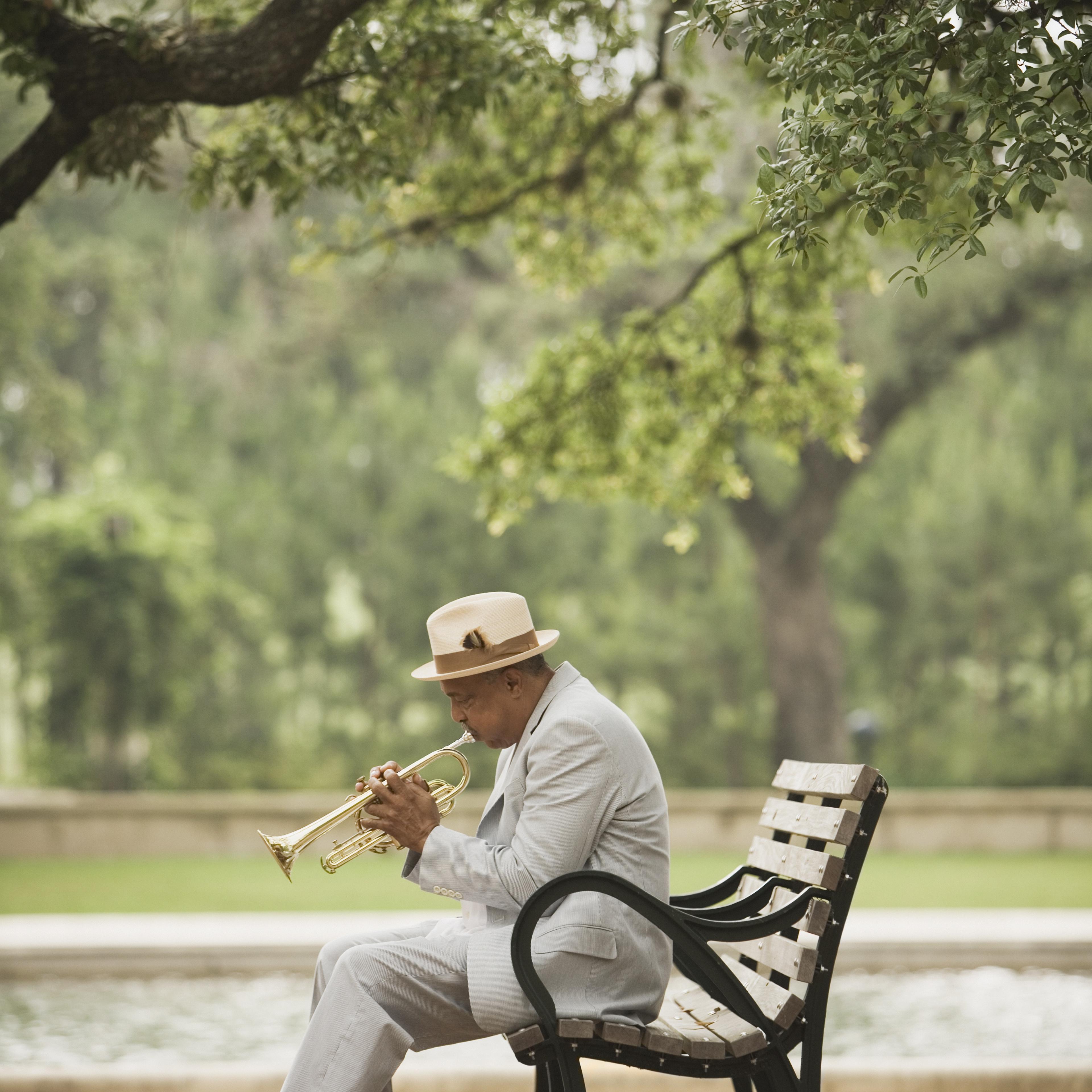man-playing-trumpet-park-bench