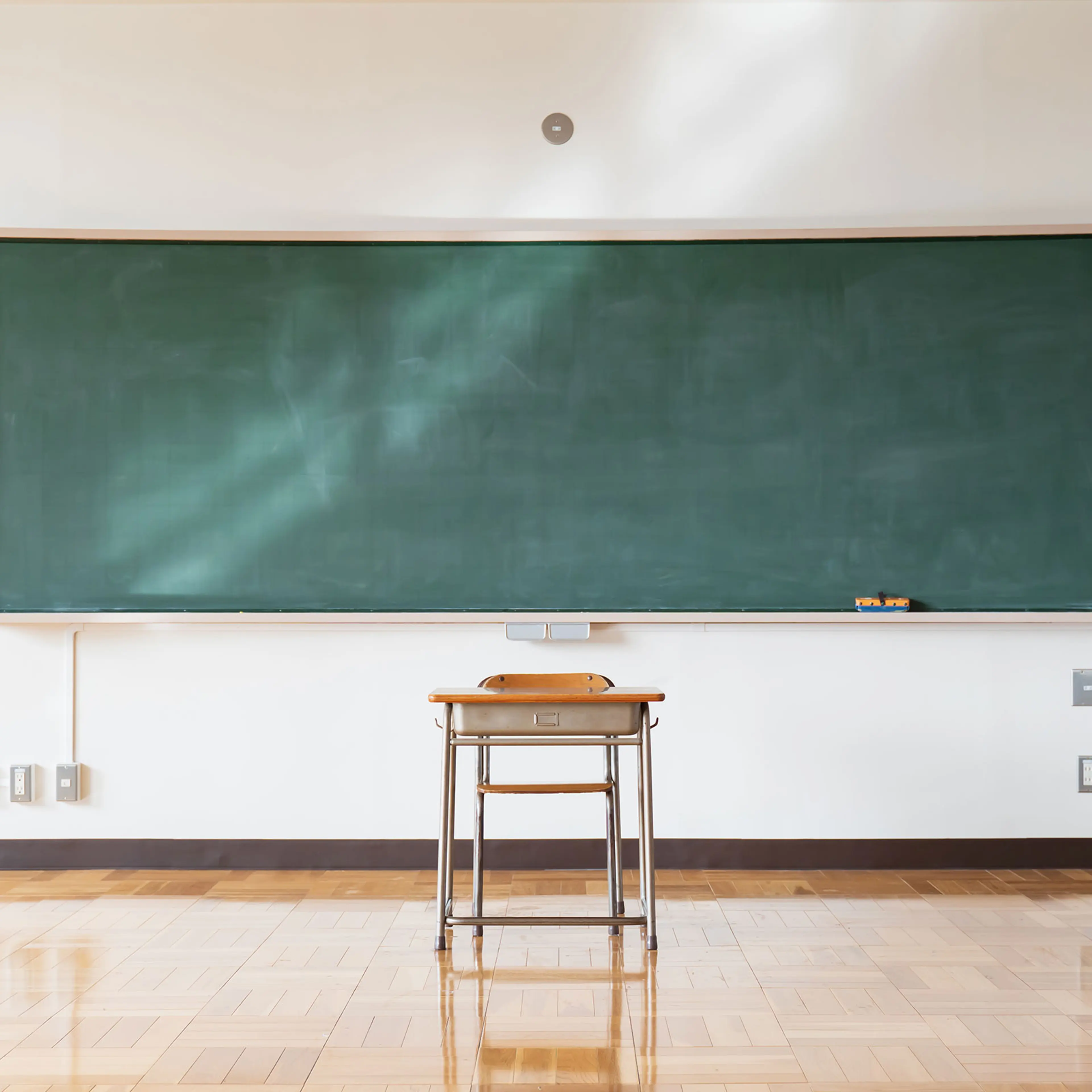 A single desk sitting in front of a blackboard in a classroom