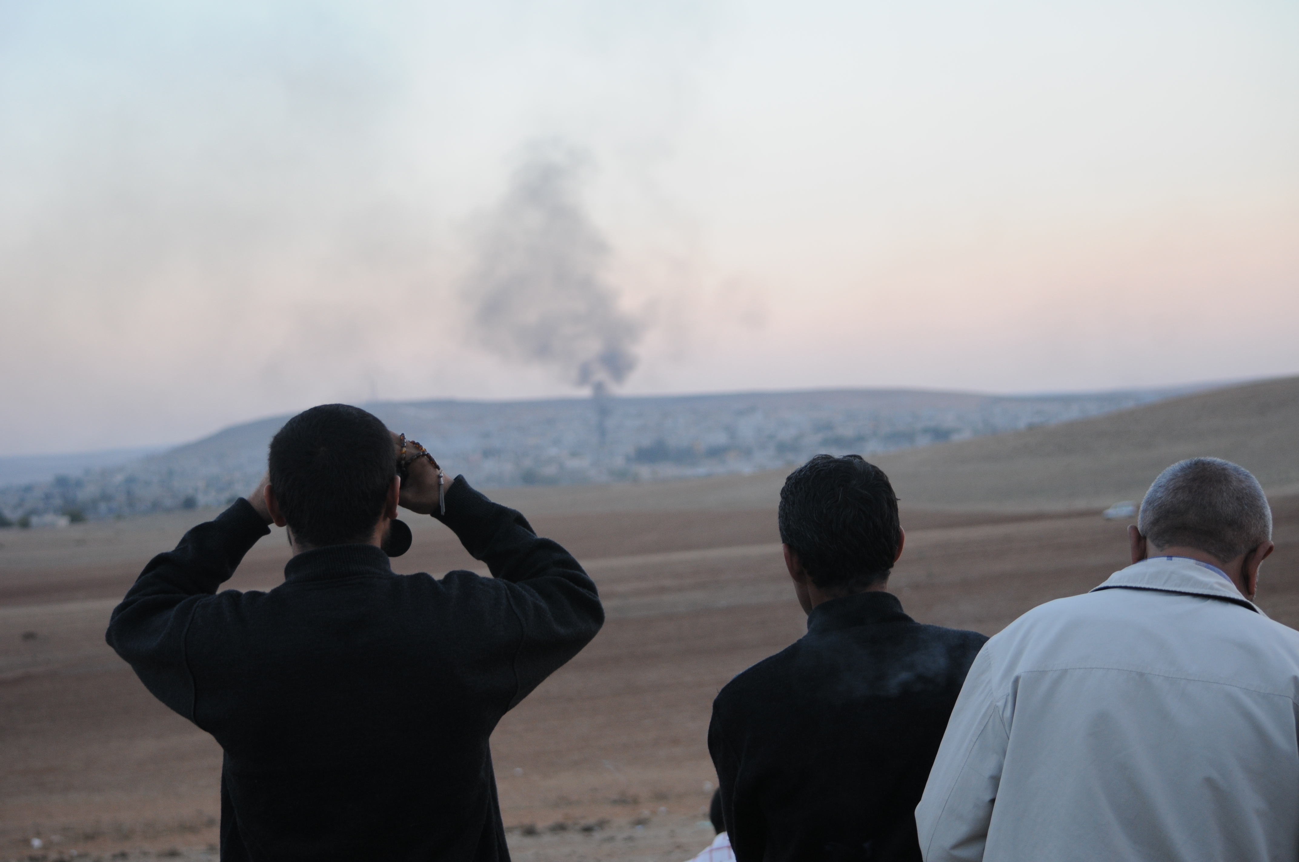 Groups of Kurdish men look at the siege of the Syrian town of Kobane from the Turkish border.