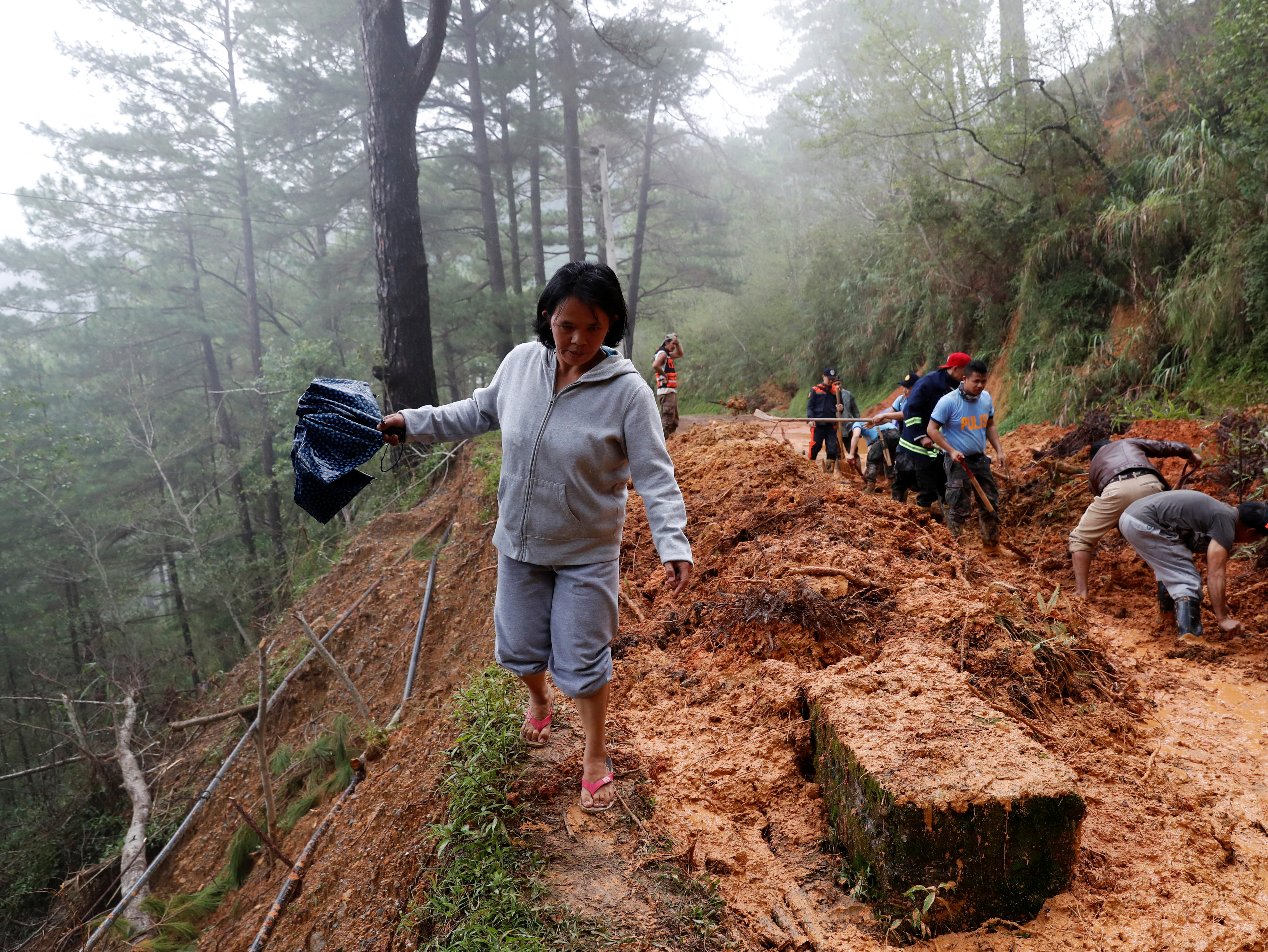 A resident walks on the side of a road as police officers and fire marshals clear debris and fallen trees caused by a landslide at the height of Typhoon Mangkhut that hit Bokod, Benguet
