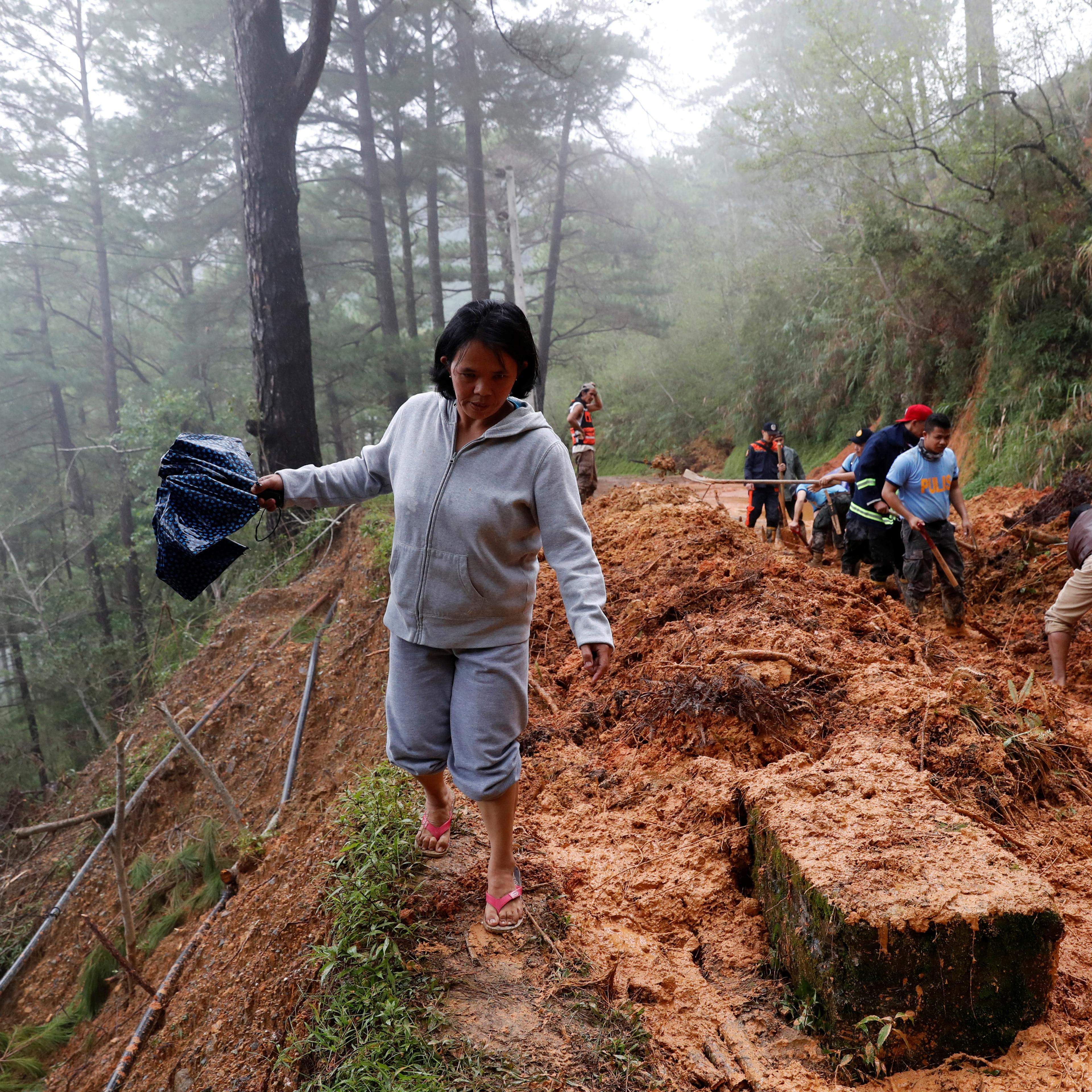 A resident walks on the side of a road as police officers and fire marshals clear debris and fallen trees caused by a landslide at the height of Typhoon Mangkhut that hit Bokod, Benguet