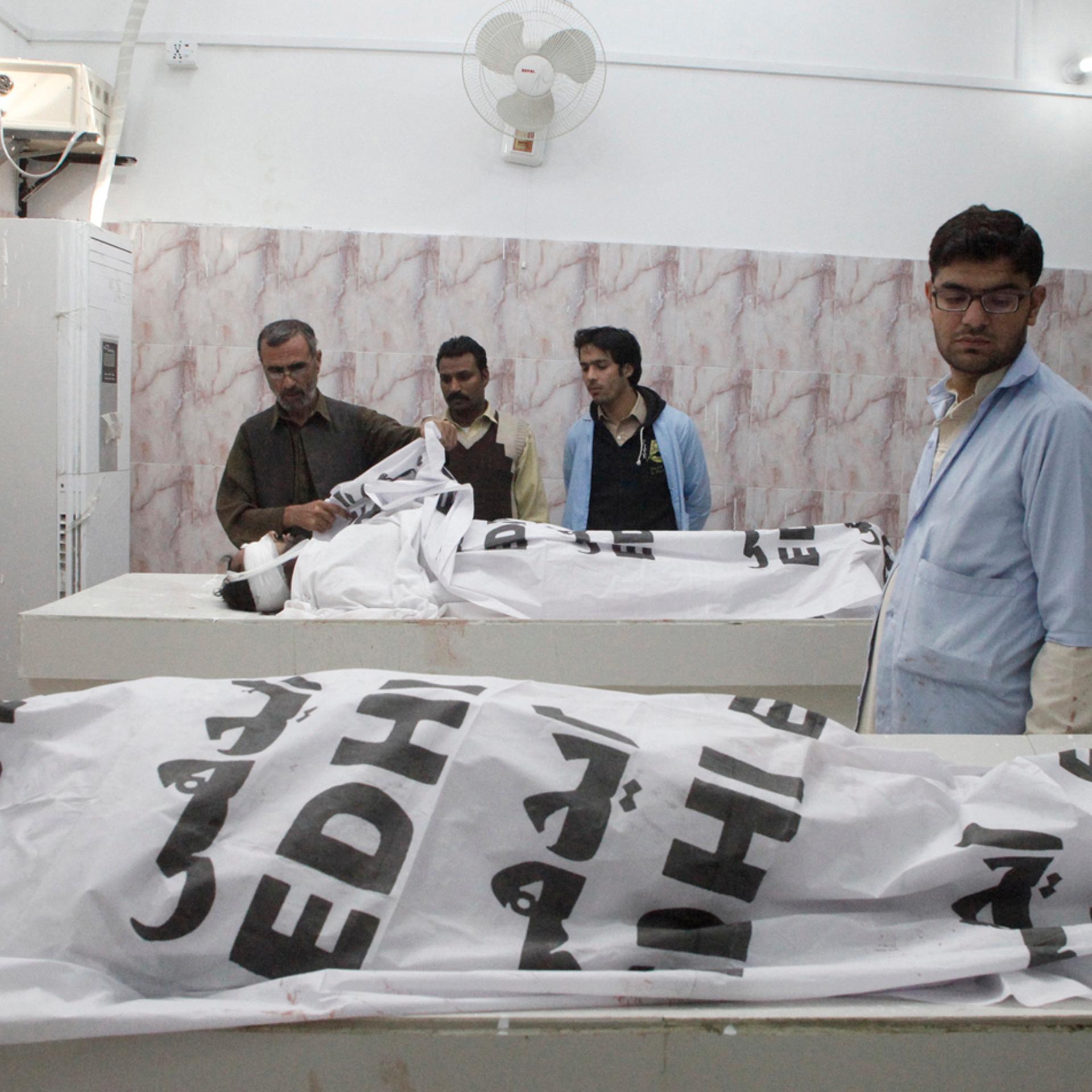 Hospital staff stand near the bodies of anti-polio drive campaign workers who were shot by gunmen, at a hospital morgue in Quetta