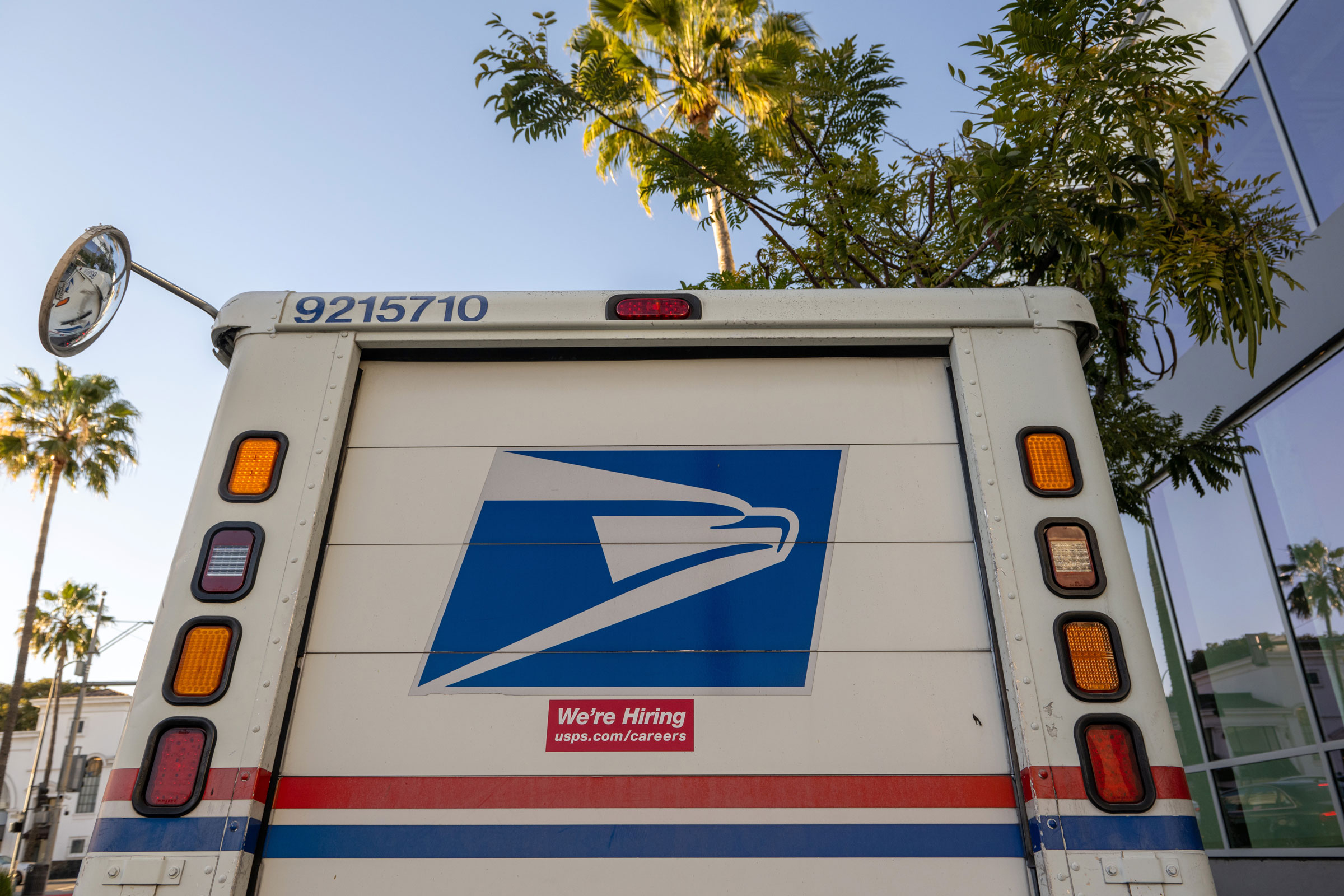 A "We're Hiring" sticker is displayed on a USPS postal truck in Beverly Hills