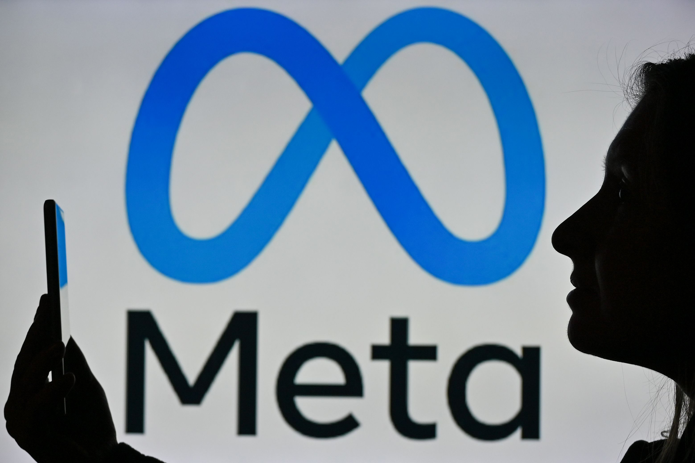 A woman in Edmonton, Canada holds a cell phone in front of a Meta logo, January 2022.