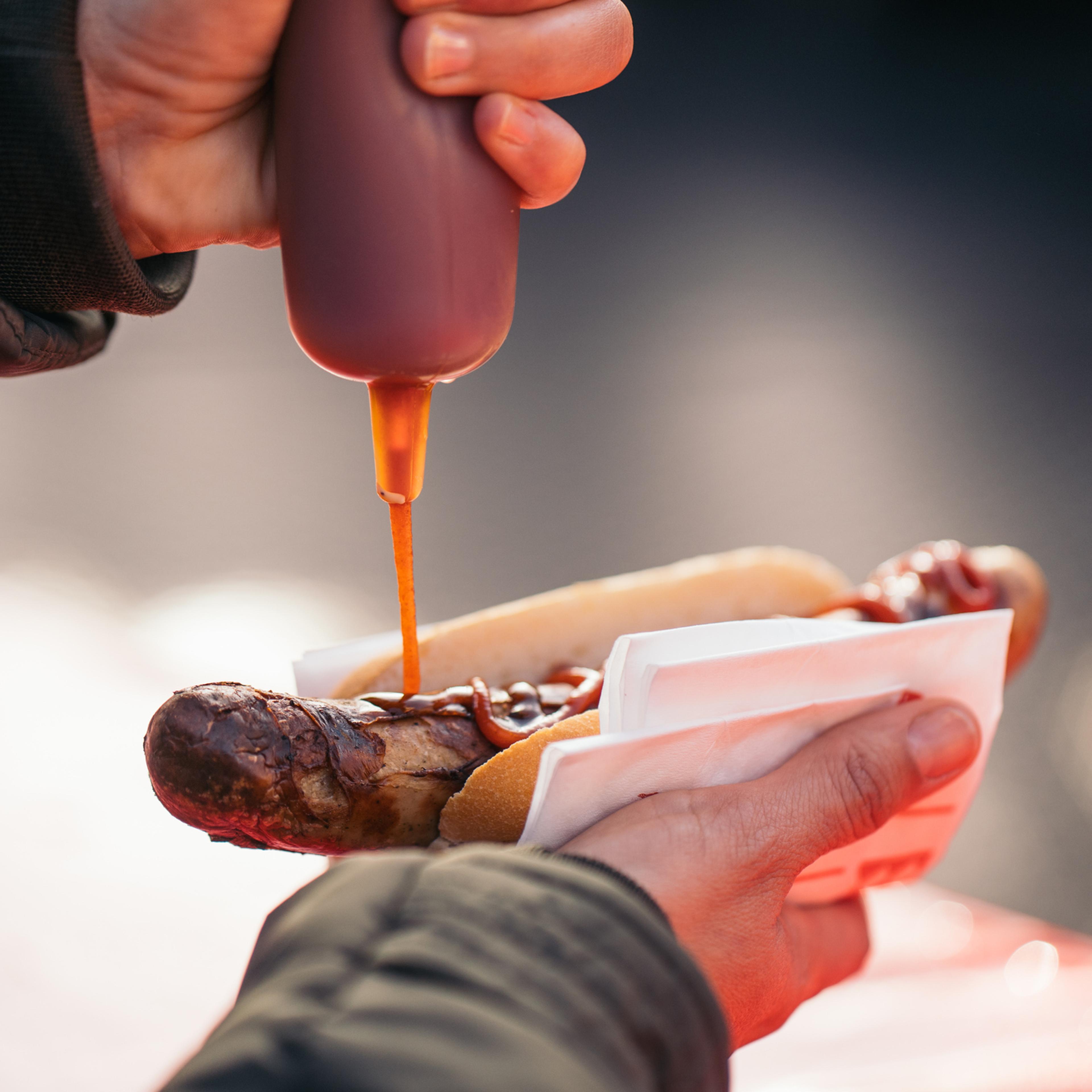 Woman pouring tomato sauce, mayonnaise and mustard on a grilled pork sausage Bratwurst at a German Market.