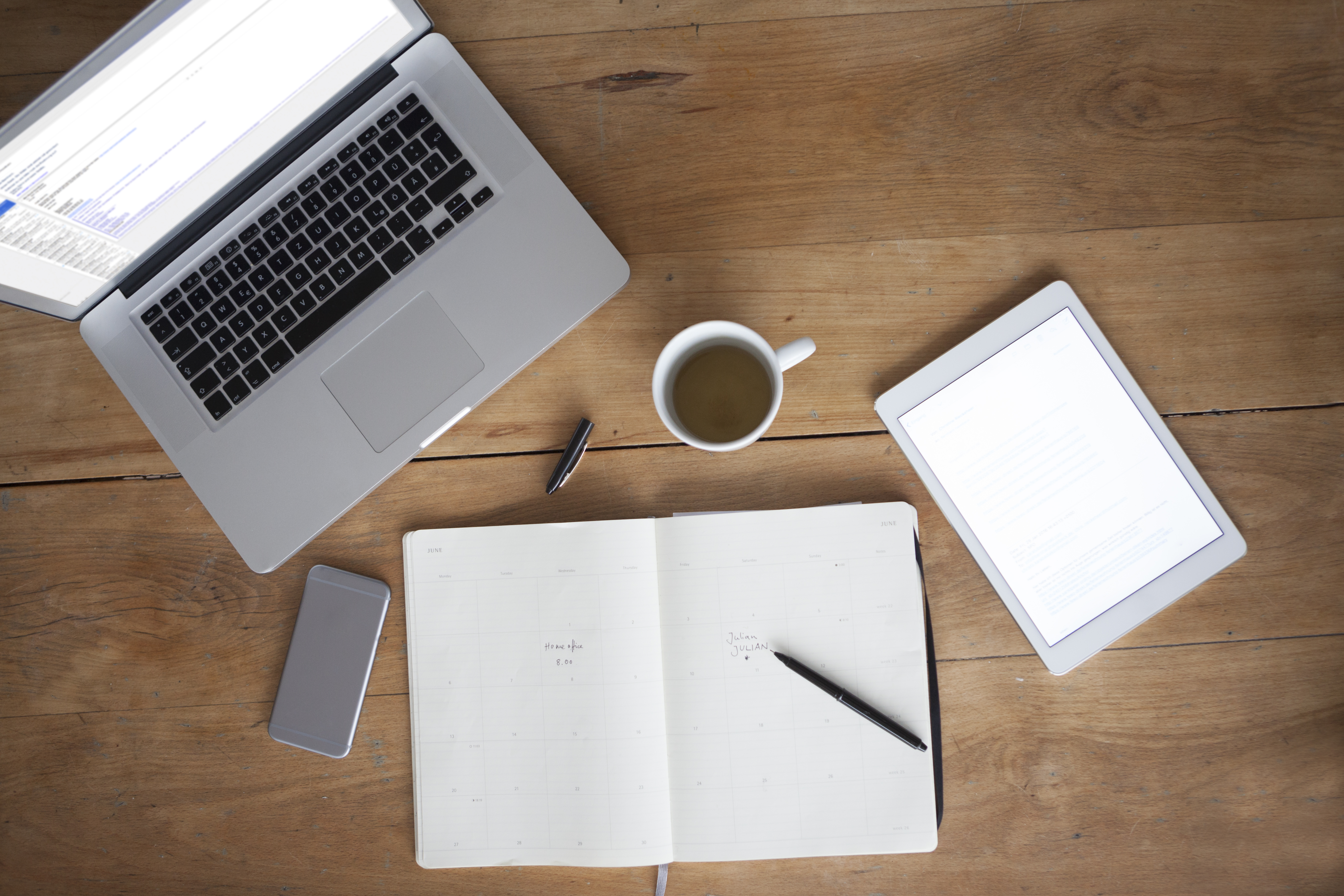 Woman at wooden table using smartphone and writing in notebook