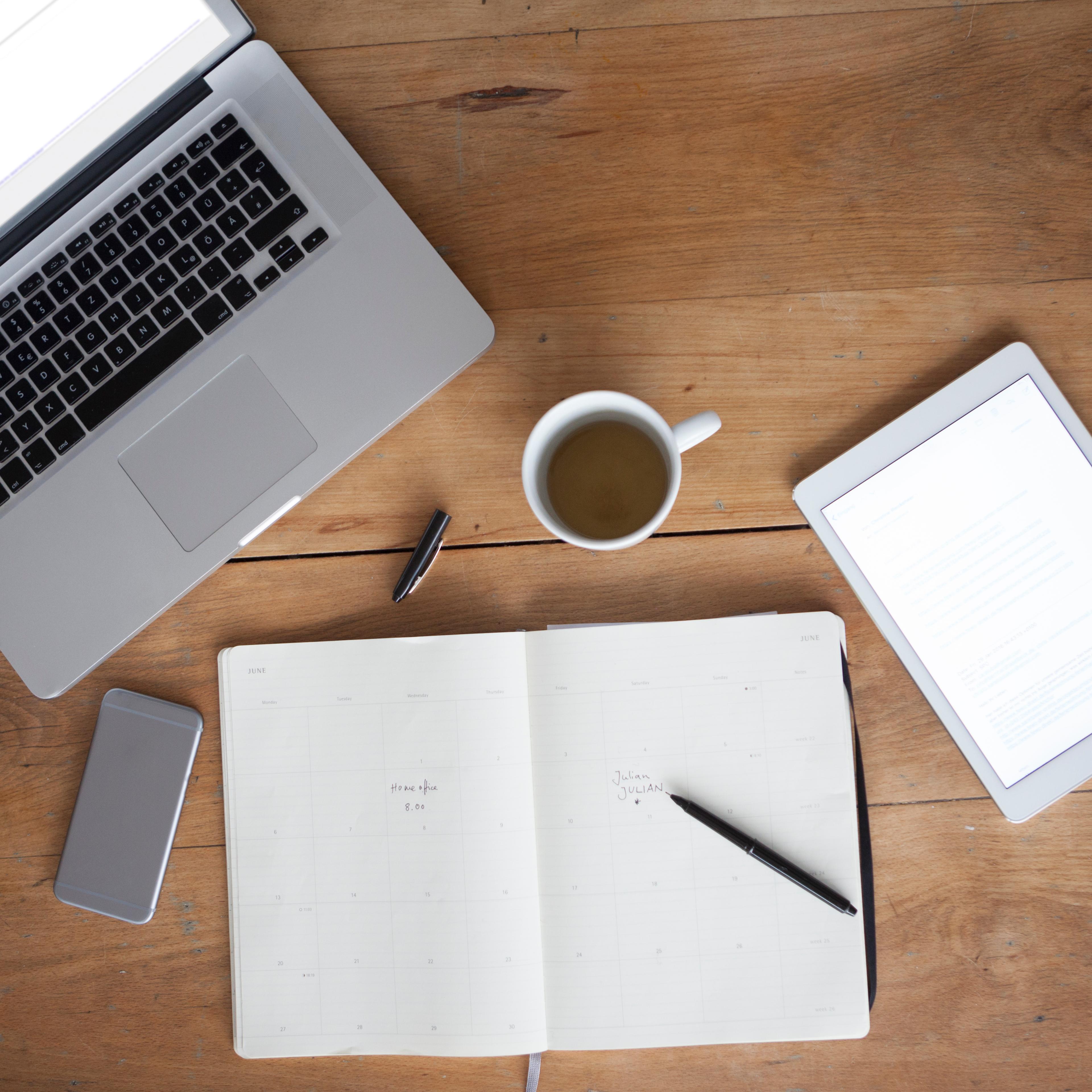 Woman at wooden table using smartphone and writing in notebook