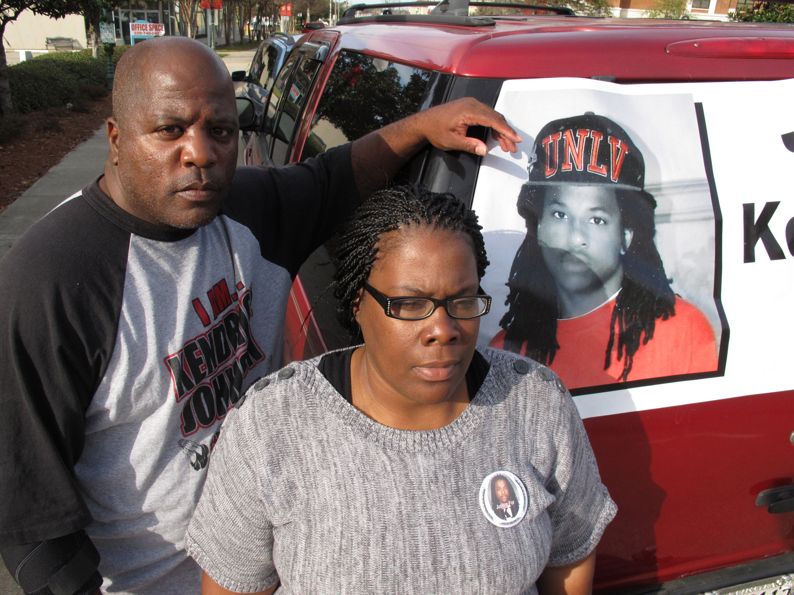 FILE- In this Dec. 13, 2013 file photo, Kenneth and Jacquelyn Johnson stand next to a banner on their SUV showing their late son, Kendrick Johnson in Valdosta, Ga. The parents of Kendrick Johnson, who was found dead inside a rolled-up gym mat at school, 