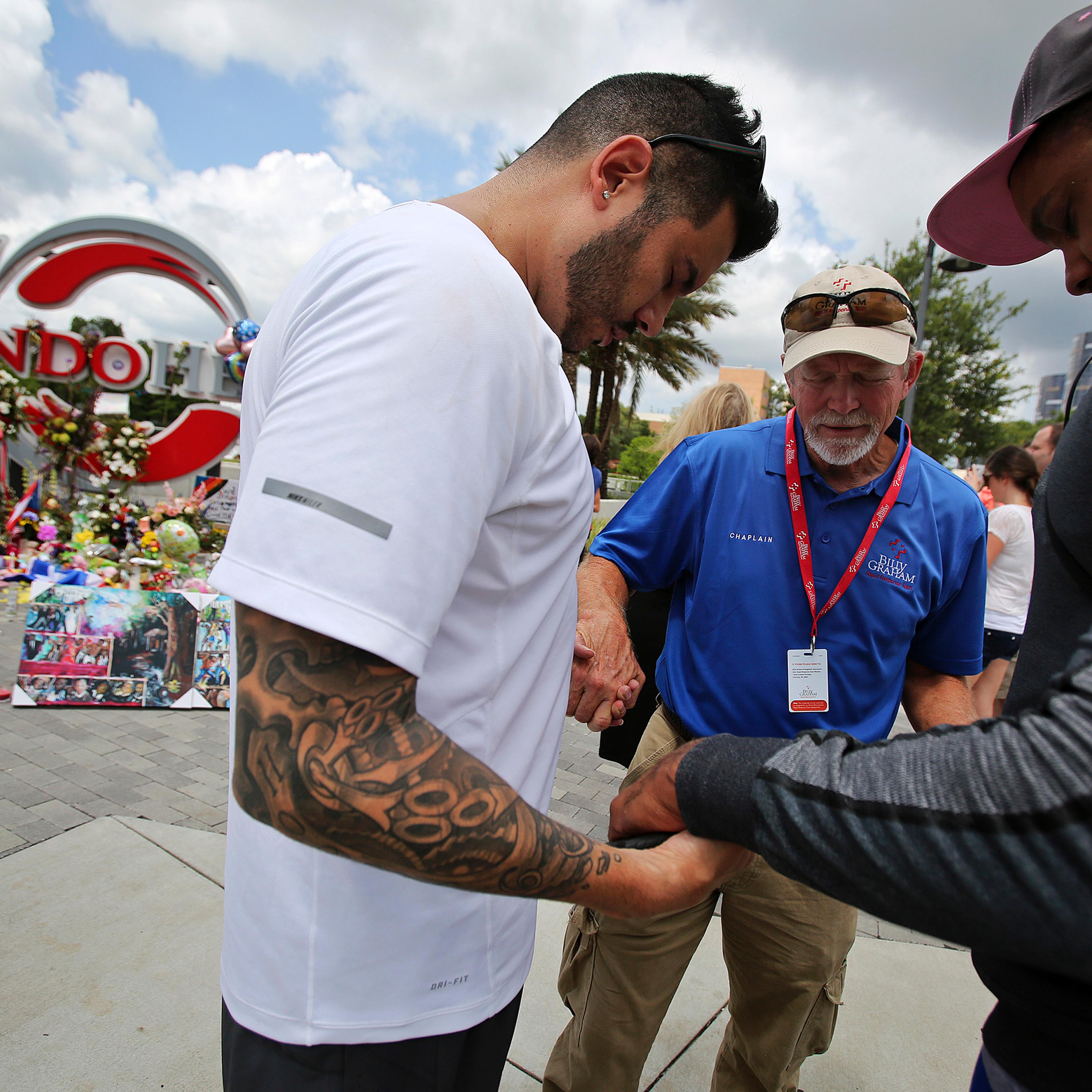 Carl Hill, center, with the Billy Graham Rapid Response Team, prays with Ricky Padilla, left, and Nathan Watson, right, by a memorial set up at the Orlando Health sign at the corner of Orange Avenue and Miller Street in Orlando on June 16, 2016.