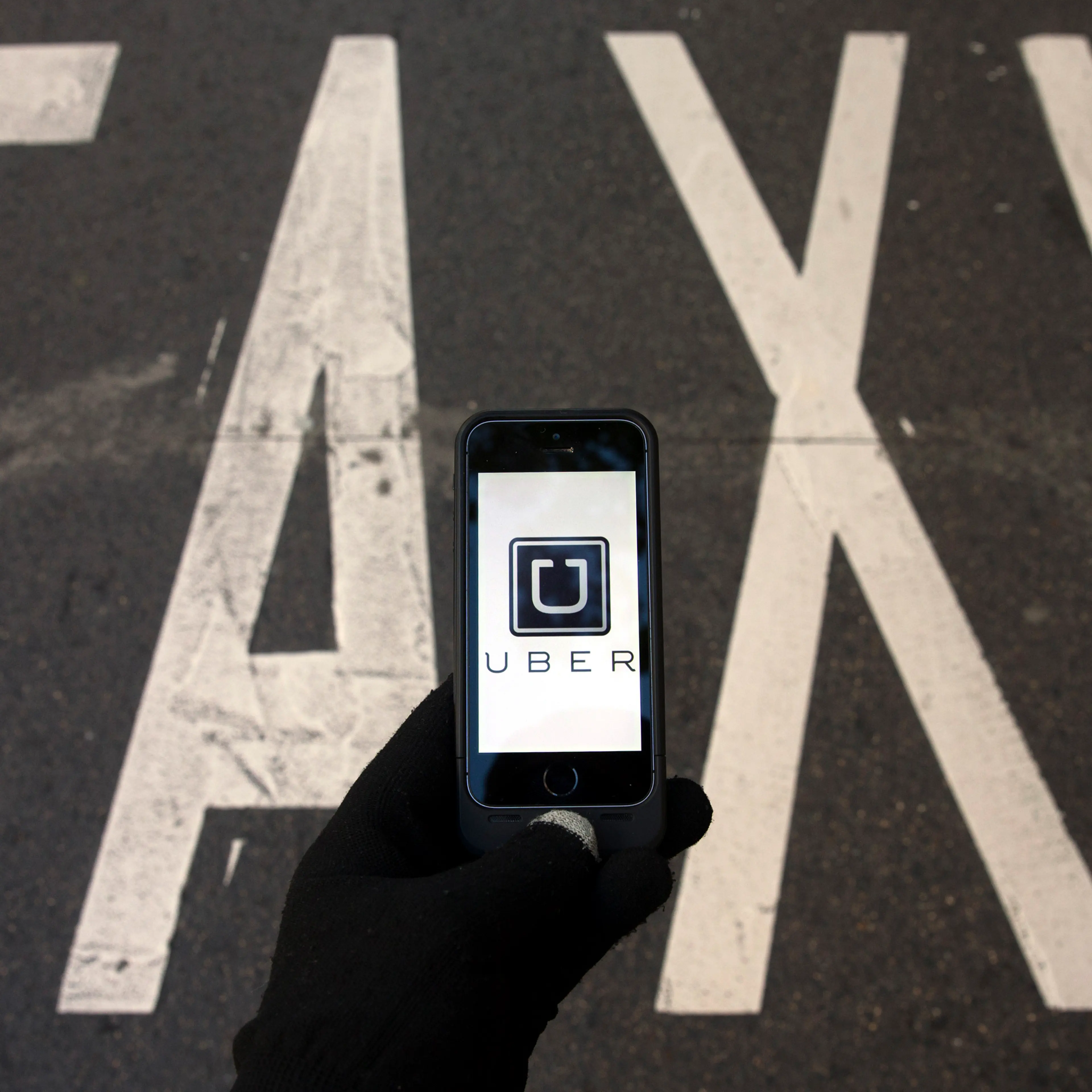 Photo illustration of logo of car-sharing service app Uber on a smartphone over a reserved lane for taxis in a street in Madrid