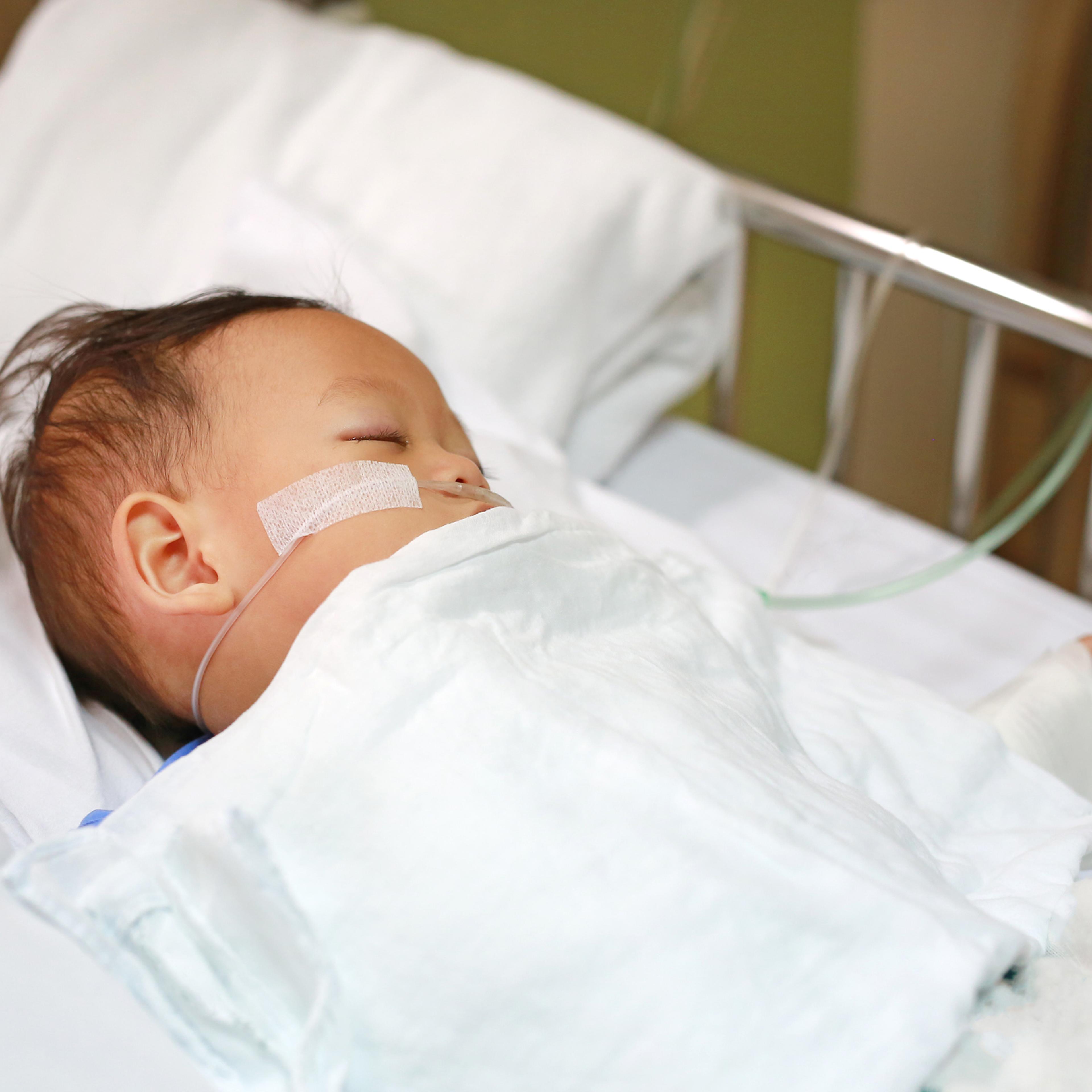 Baby boy with breathing tube in nose receiving medical treatment. Intensive care and attaching intravenous tube to hand on bed at hospital. Respiratory Syncytial Virus (RSV).