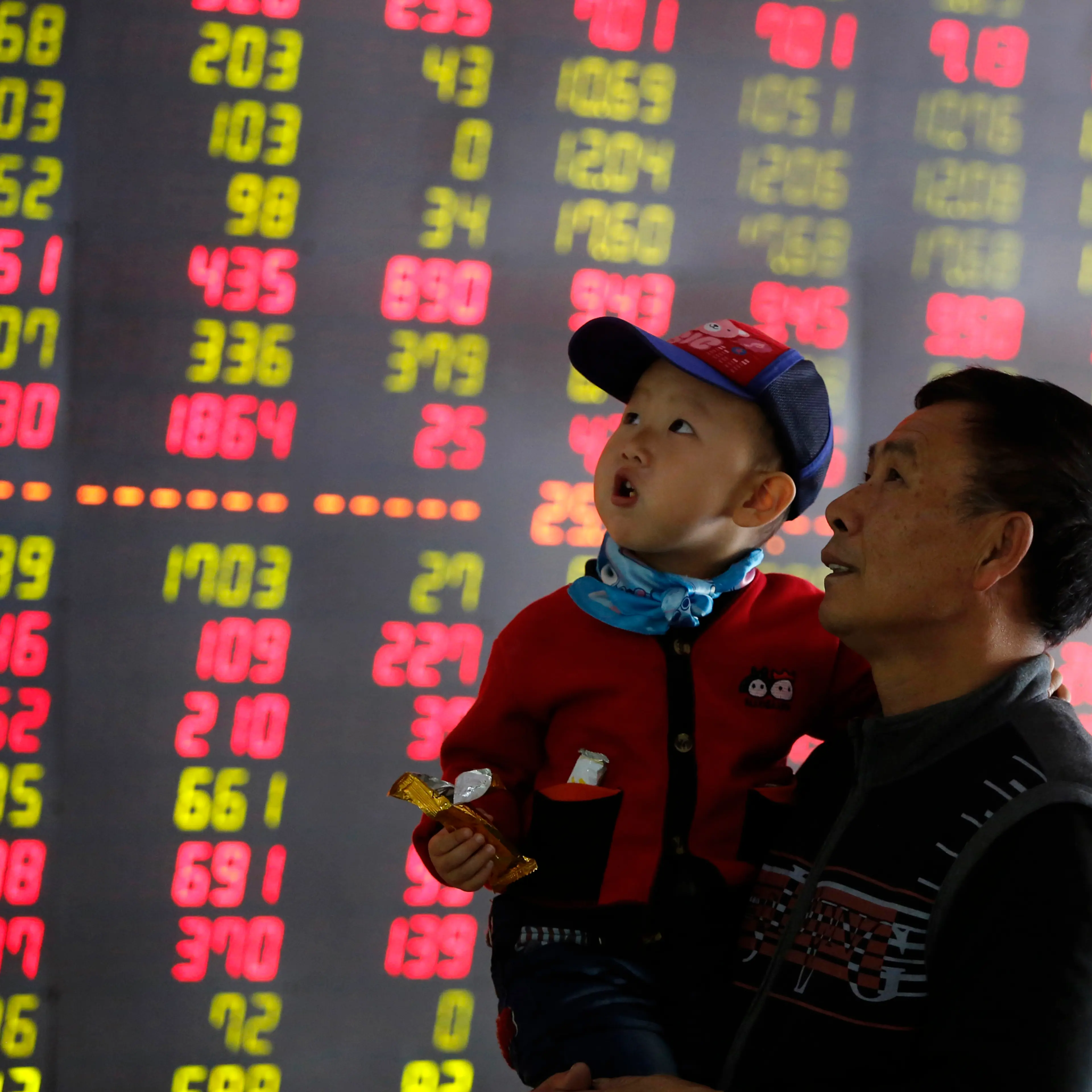 An investor holds a child in front of an electronic screen showing stock information at a brokerage house in Shenyang