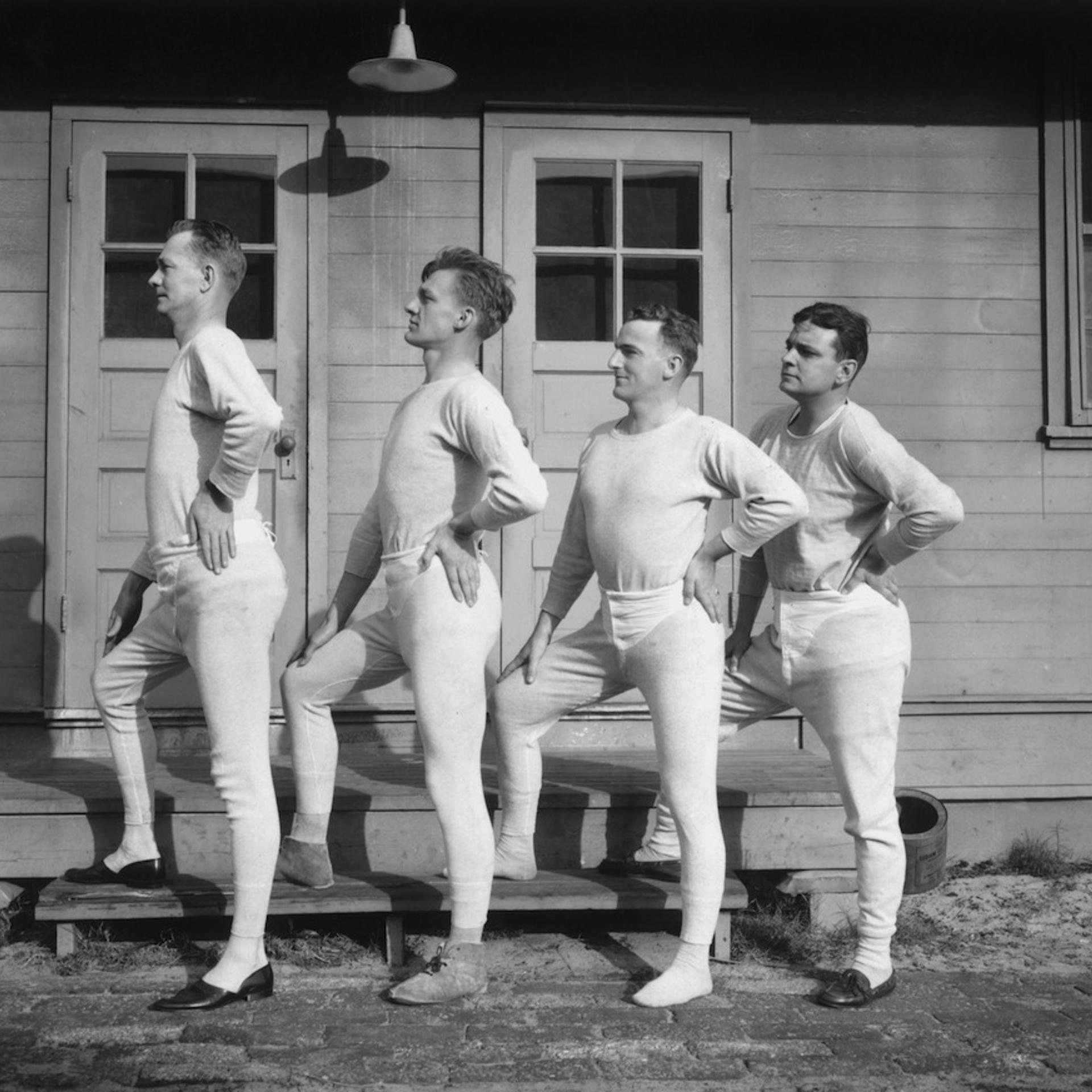 Four men wearing long underwear pose in a profile lineup, circa 1915.