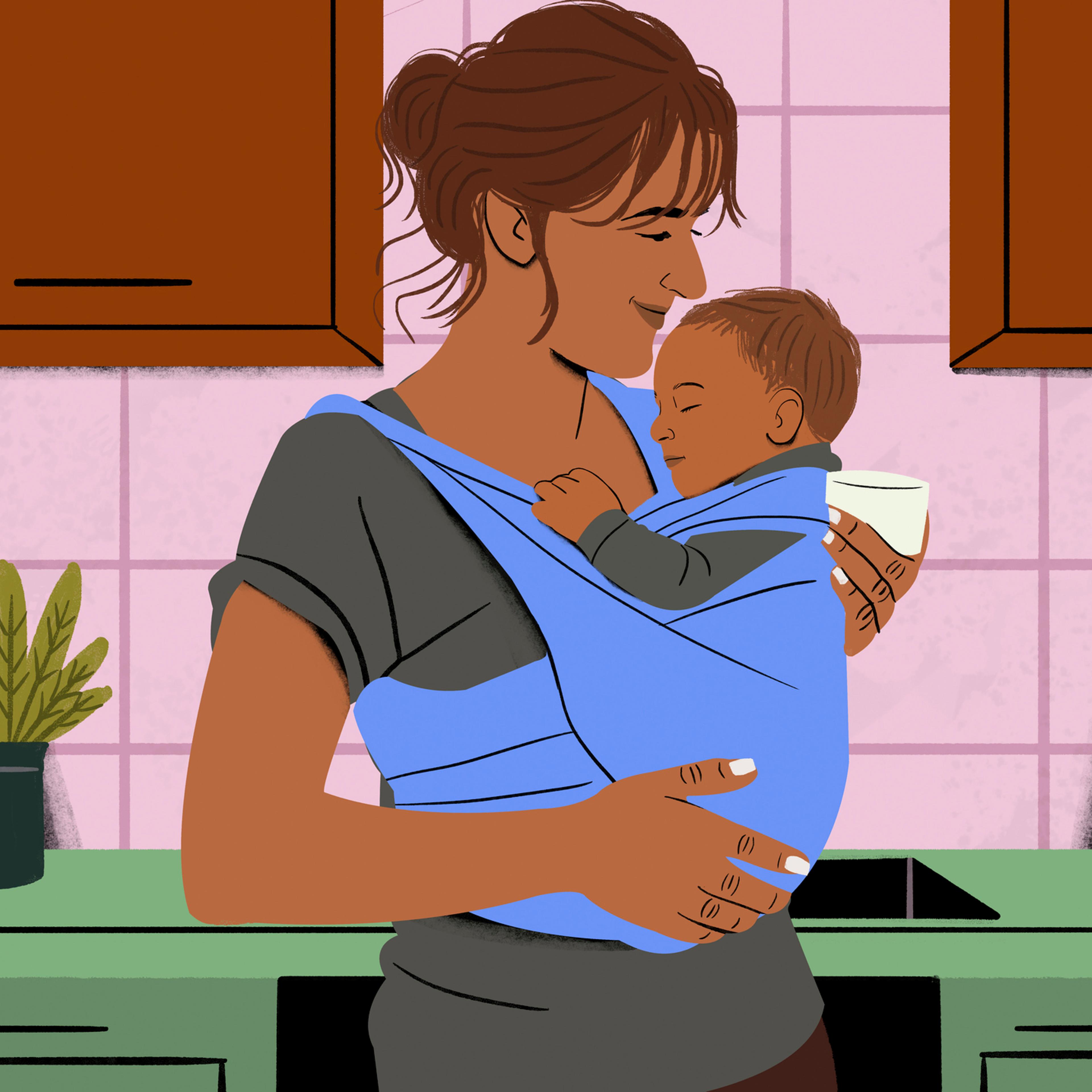 Smiling woman holding a sleeping baby in a blue sling in a cozy kitchen setting