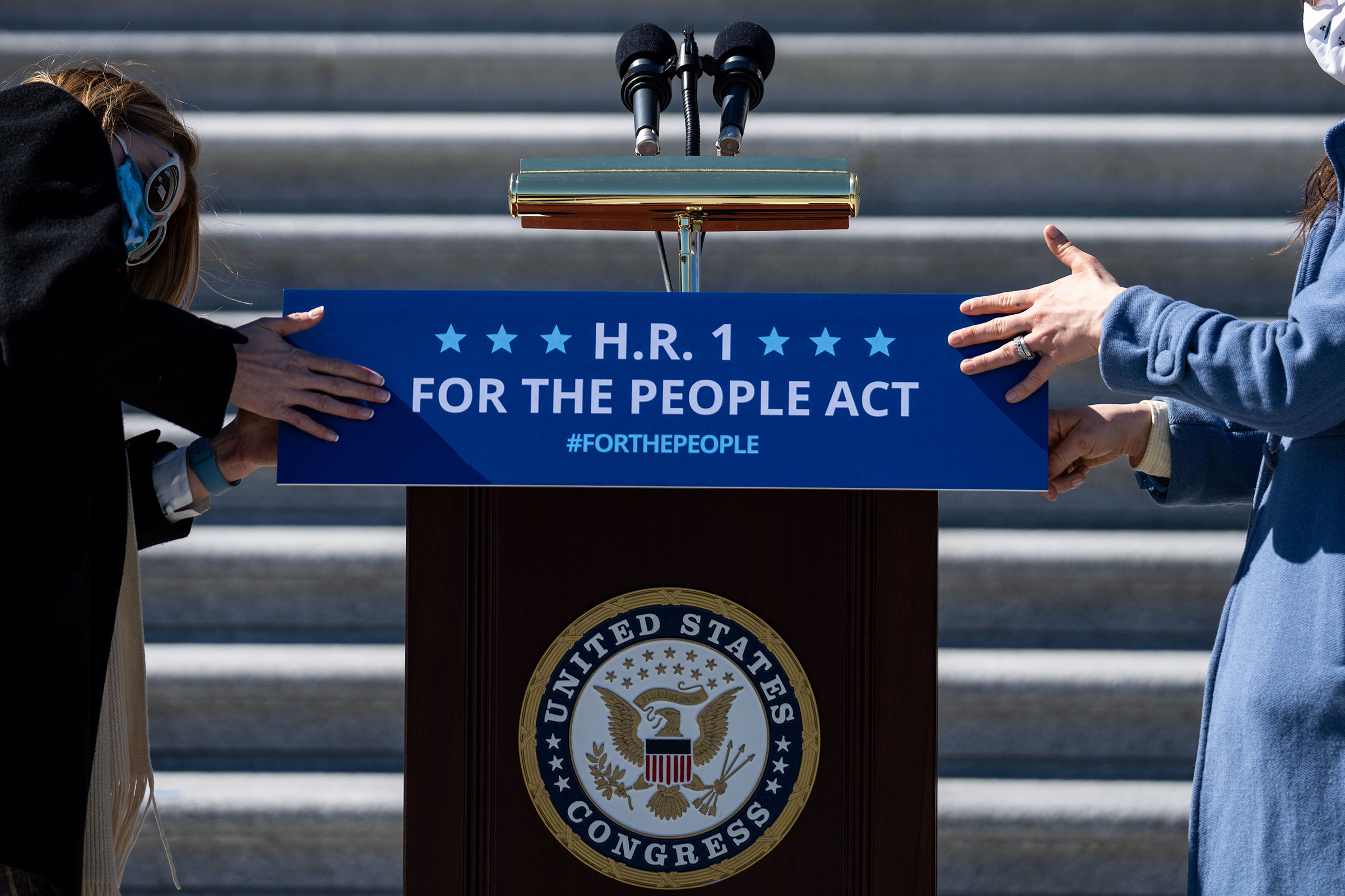 Staffers place a sign on a podium in preparation for a news conference with House Democrats regarding H.R. 1, the For the People Act, on Capitol Hill on March 3, 2021.