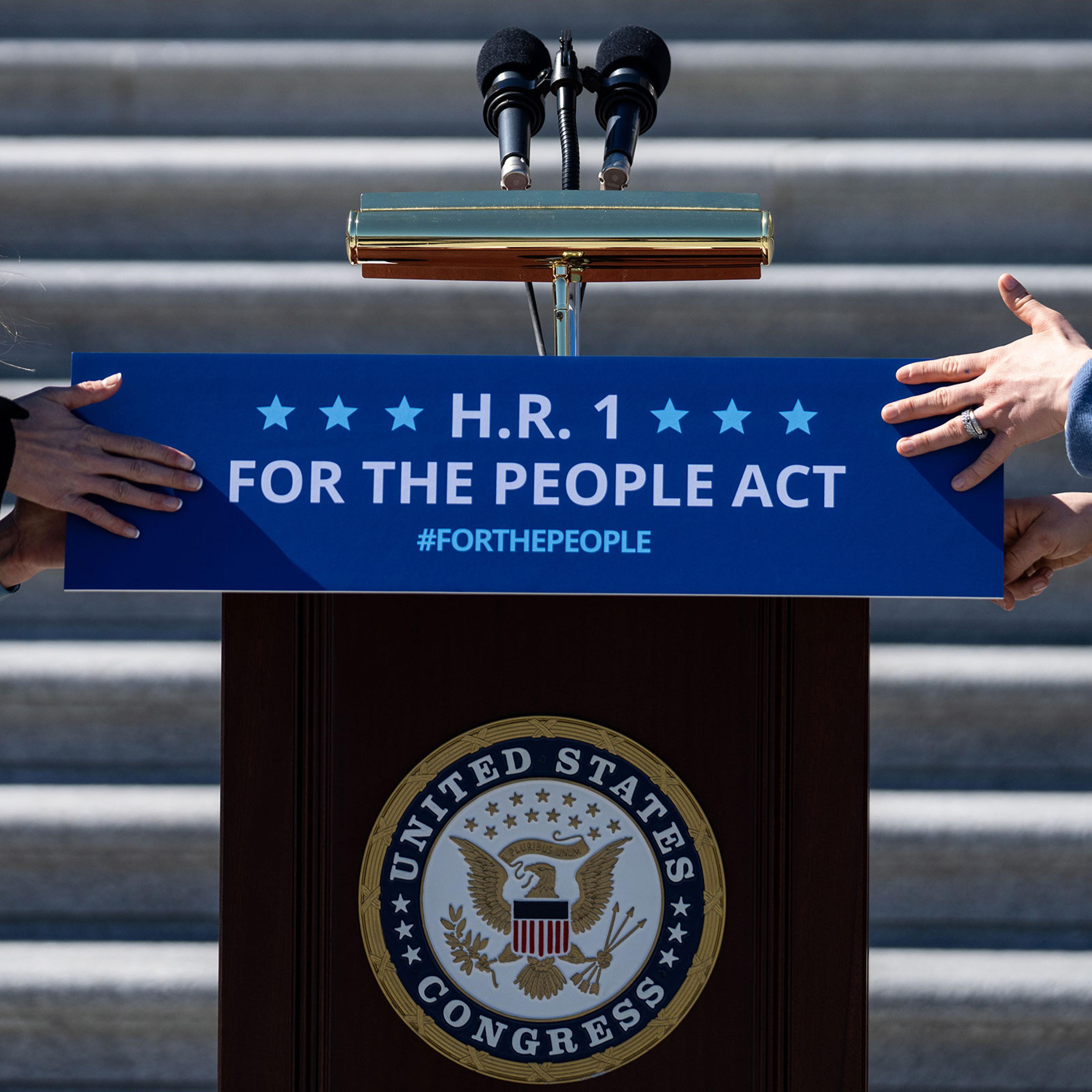 Staffers place a sign on a podium in preparation for a news conference with House Democrats regarding H.R. 1, the For the People Act, on Capitol Hill on March 3, 2021.