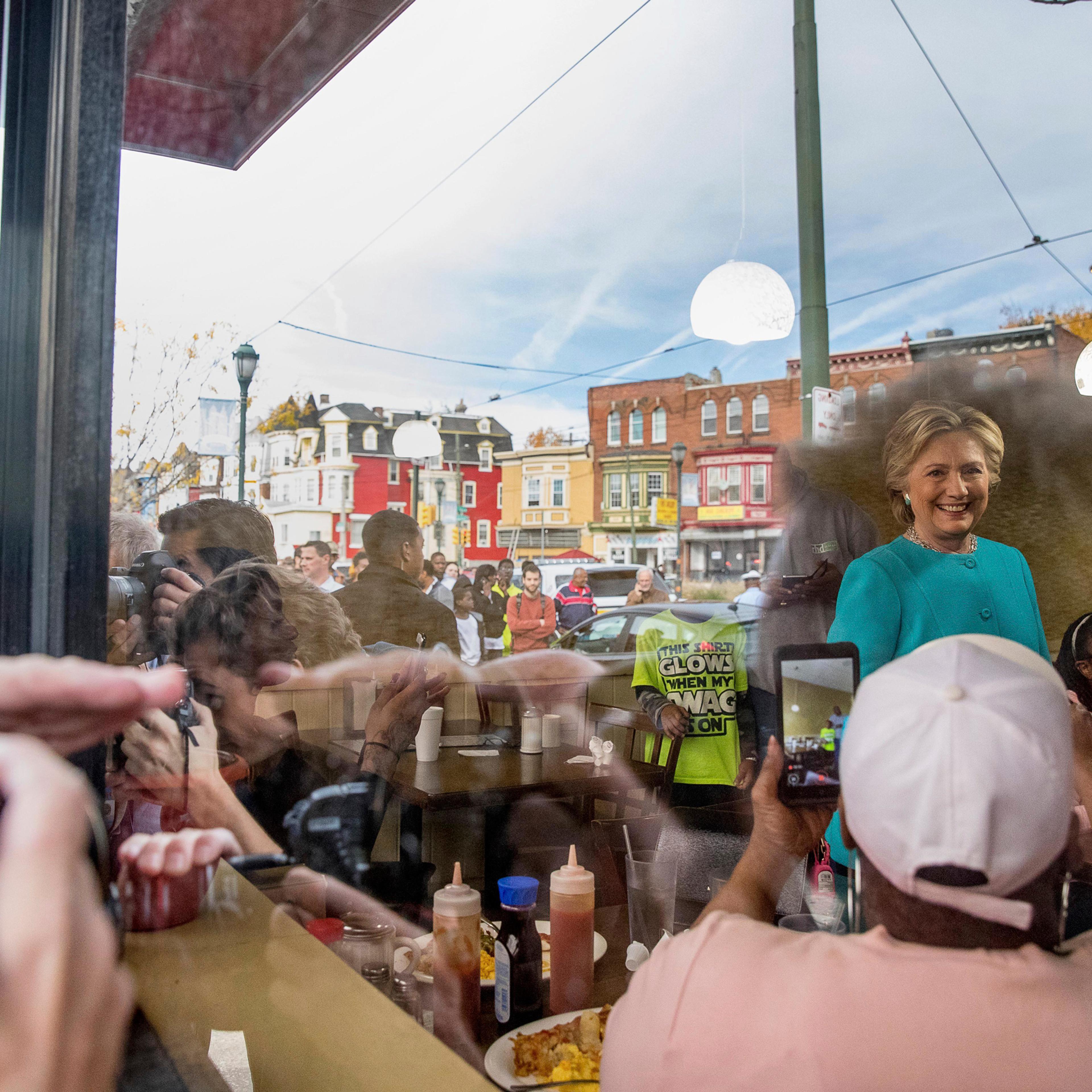 As seen through a window, Democratic presidential candidate Hillary Clinton greets patrons at Cedar Park Cafe in Philadelphia, Sunday, Nov. 6, 2016. (AP Photo/Andrew Harnik)