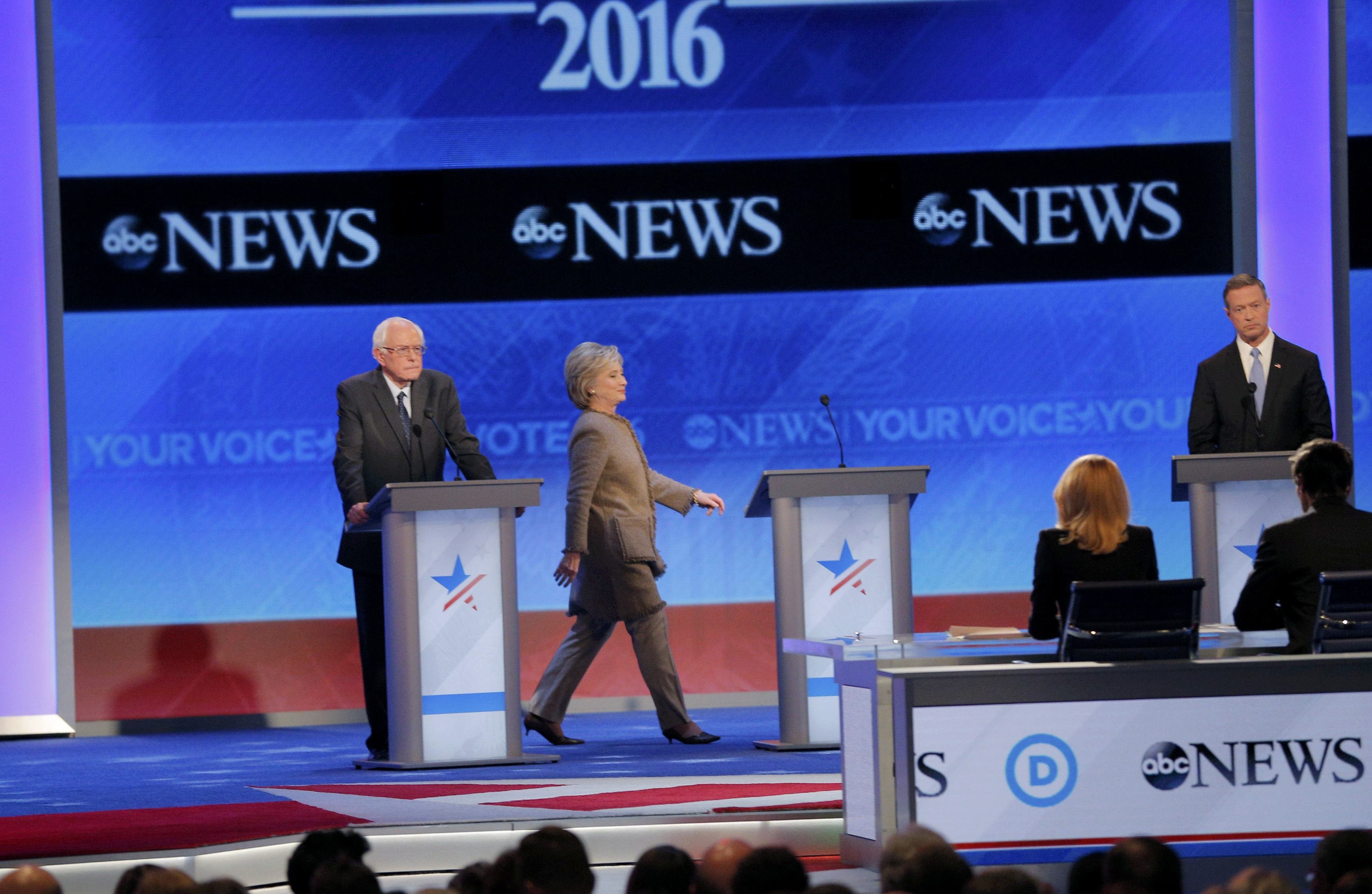 Democratic U.S. presidential candidate Clinton walks to her podium between rivals Sanders and O'Malley after she failed to return from a break in time for the resumption of the Democratic presidential candidates debate at St. Anselm College in Manchester