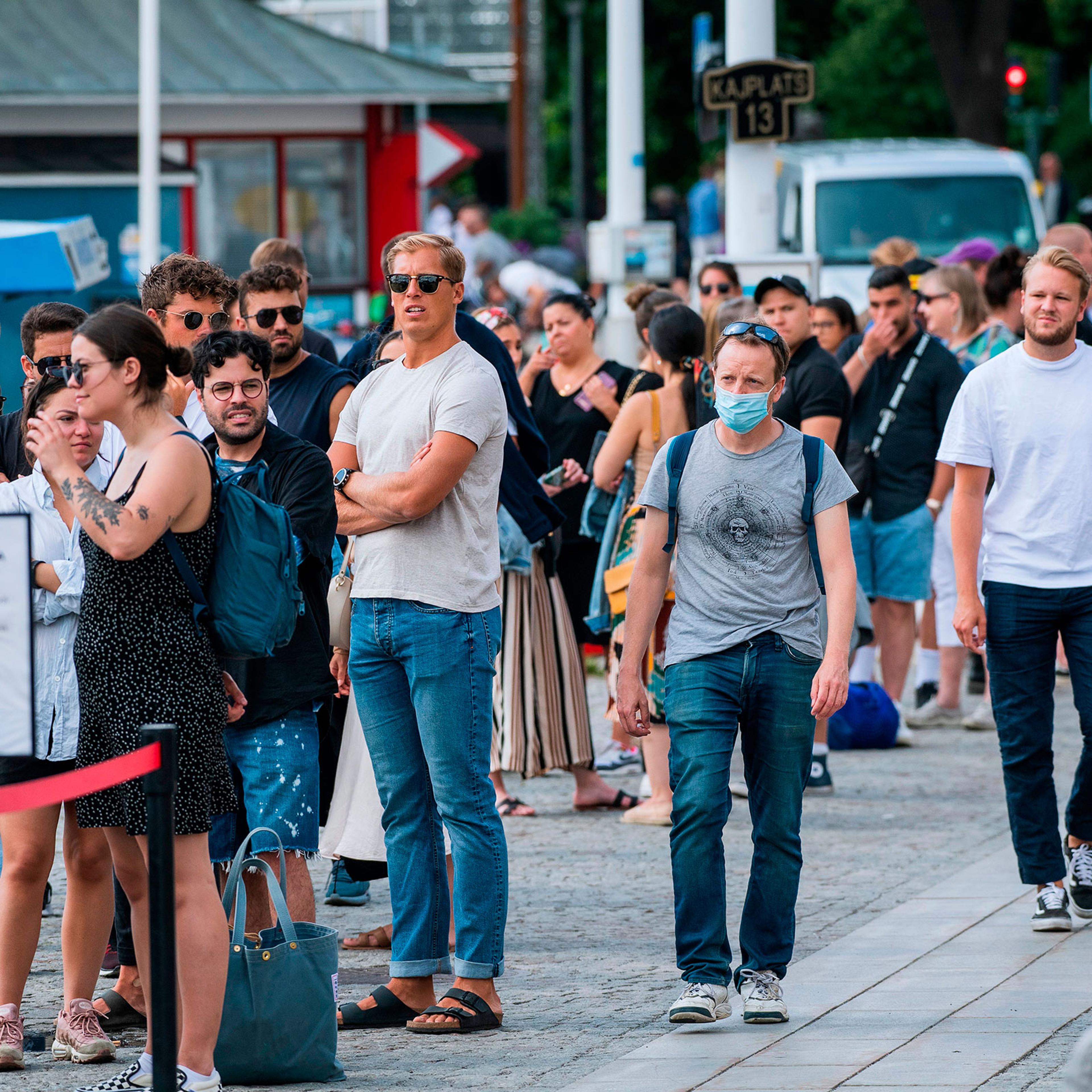 A man wearing a protective mask walks next to travelers as they queue up to board a boat in Stockholm on July 27, 2020.