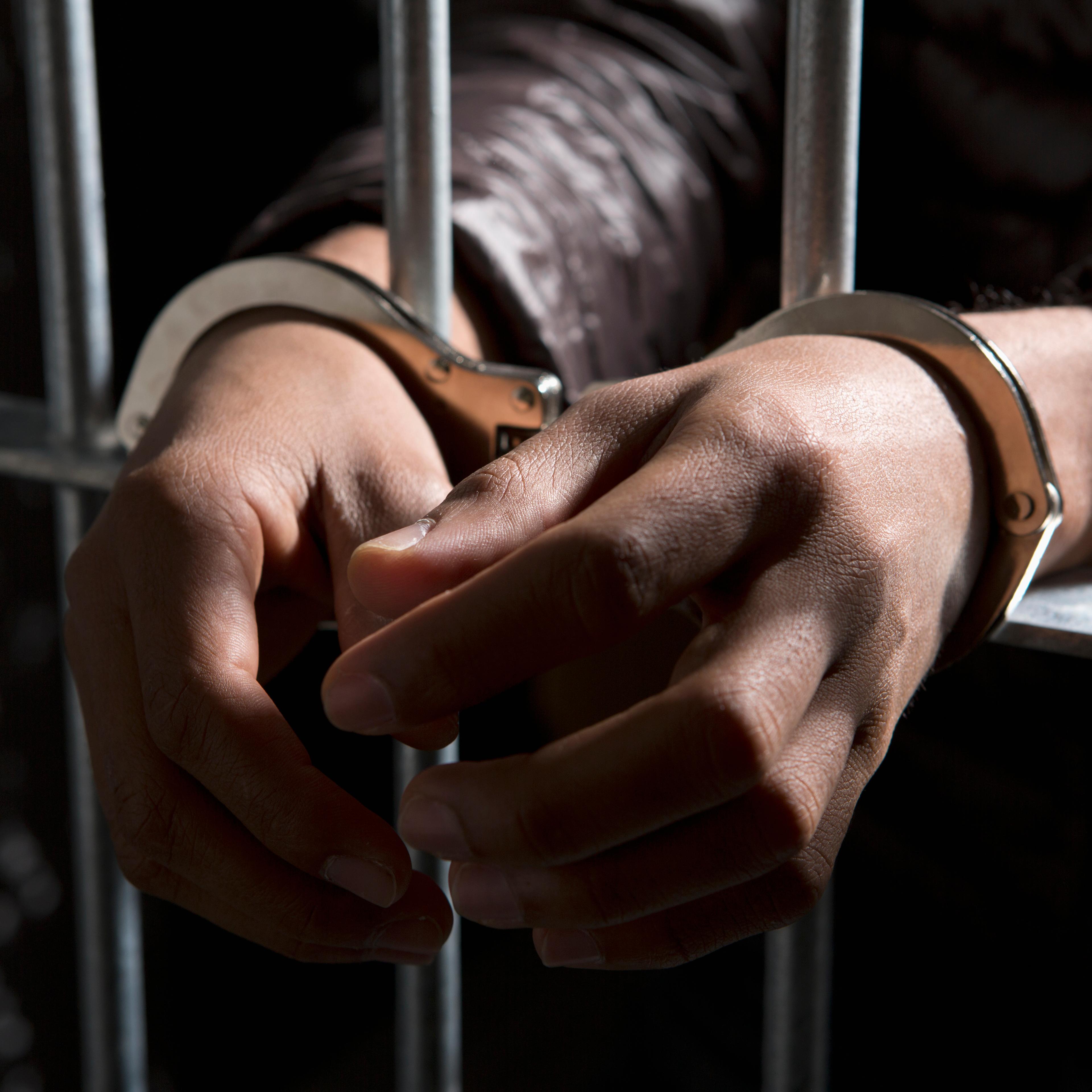 A prisoner behind bars with hands cuffed