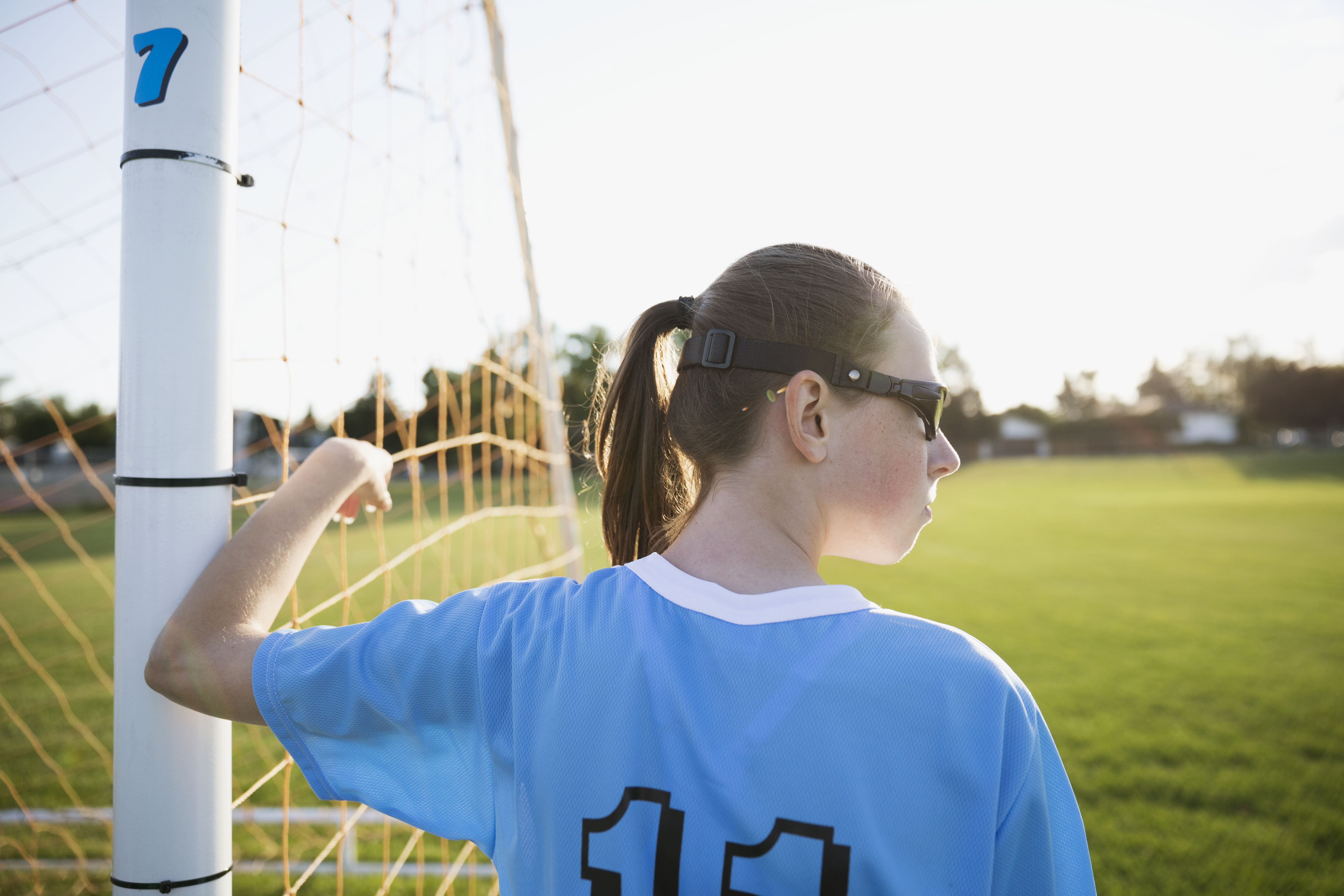 Middle school girl soccer player leaning on goal net post looking away