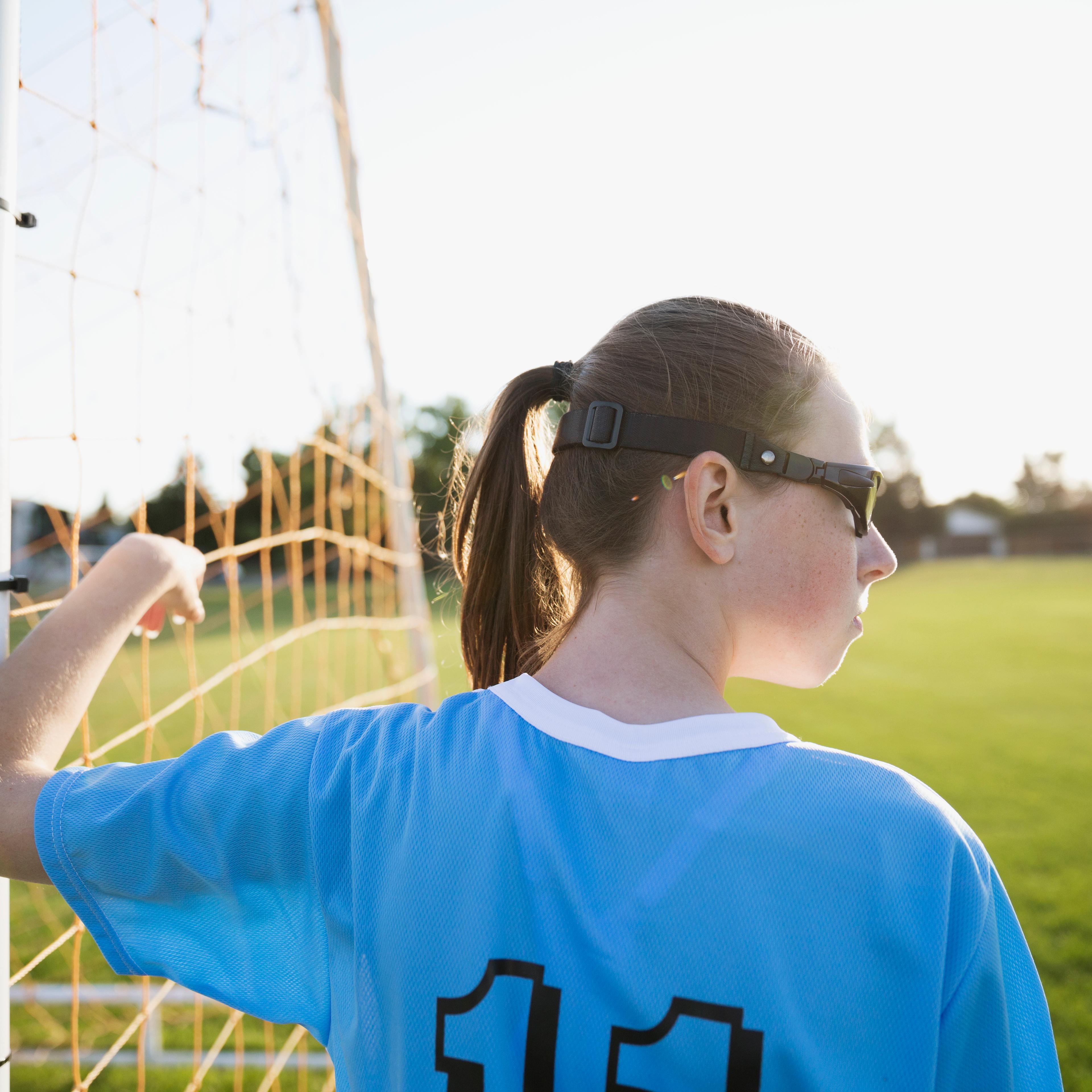 Middle school girl soccer player leaning on goal net post looking away