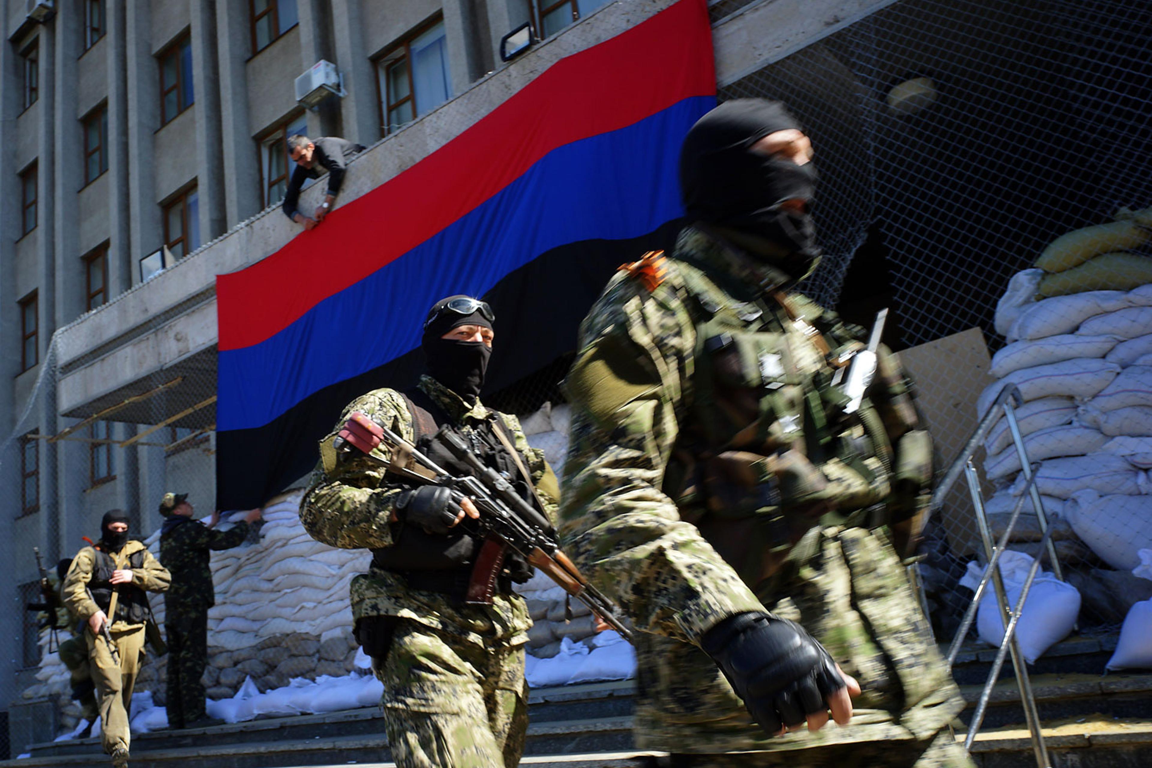 A pro-Russia activist hangs a flag of the so-called "People's Republic of Donetsk" on the regional administration building seized by separatists as armed men in military fatigues guard the premises in the eastern Ukrainian city of Slavyansk on April 21,