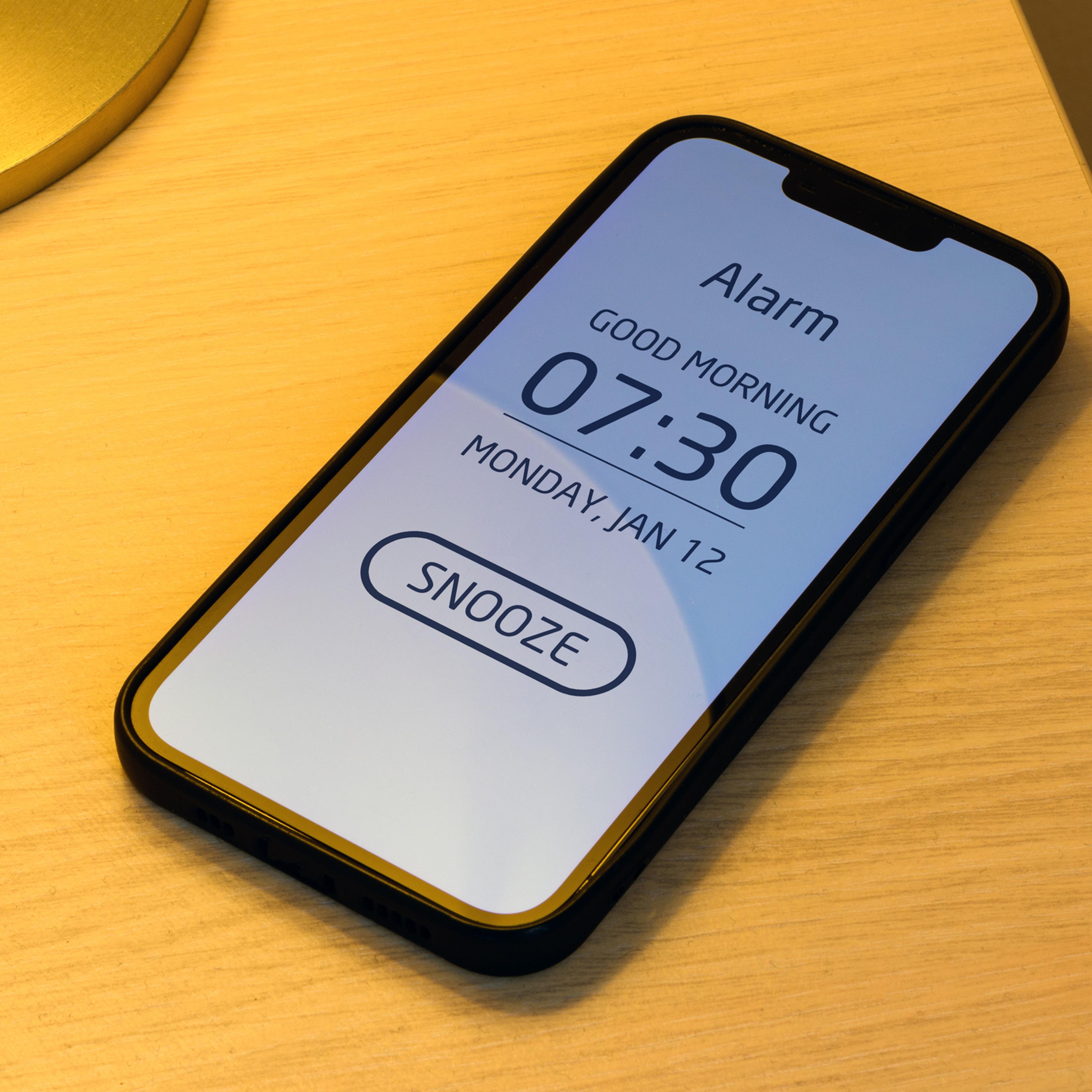 Smartphone alarm clock on bedroom night table with snooze button