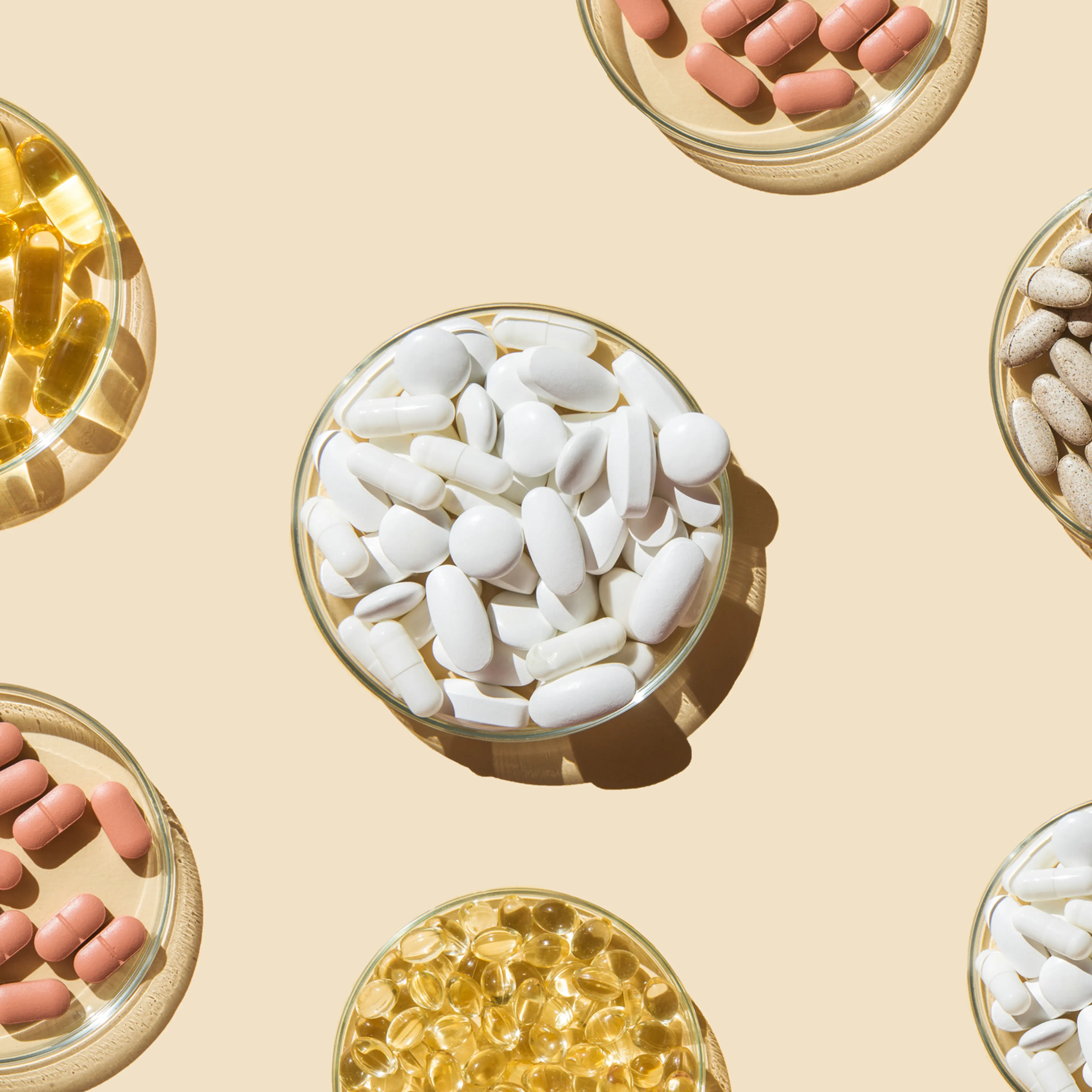 Various pills and capsules, vitamins and dietary supplements in petri dishes on a beige background.