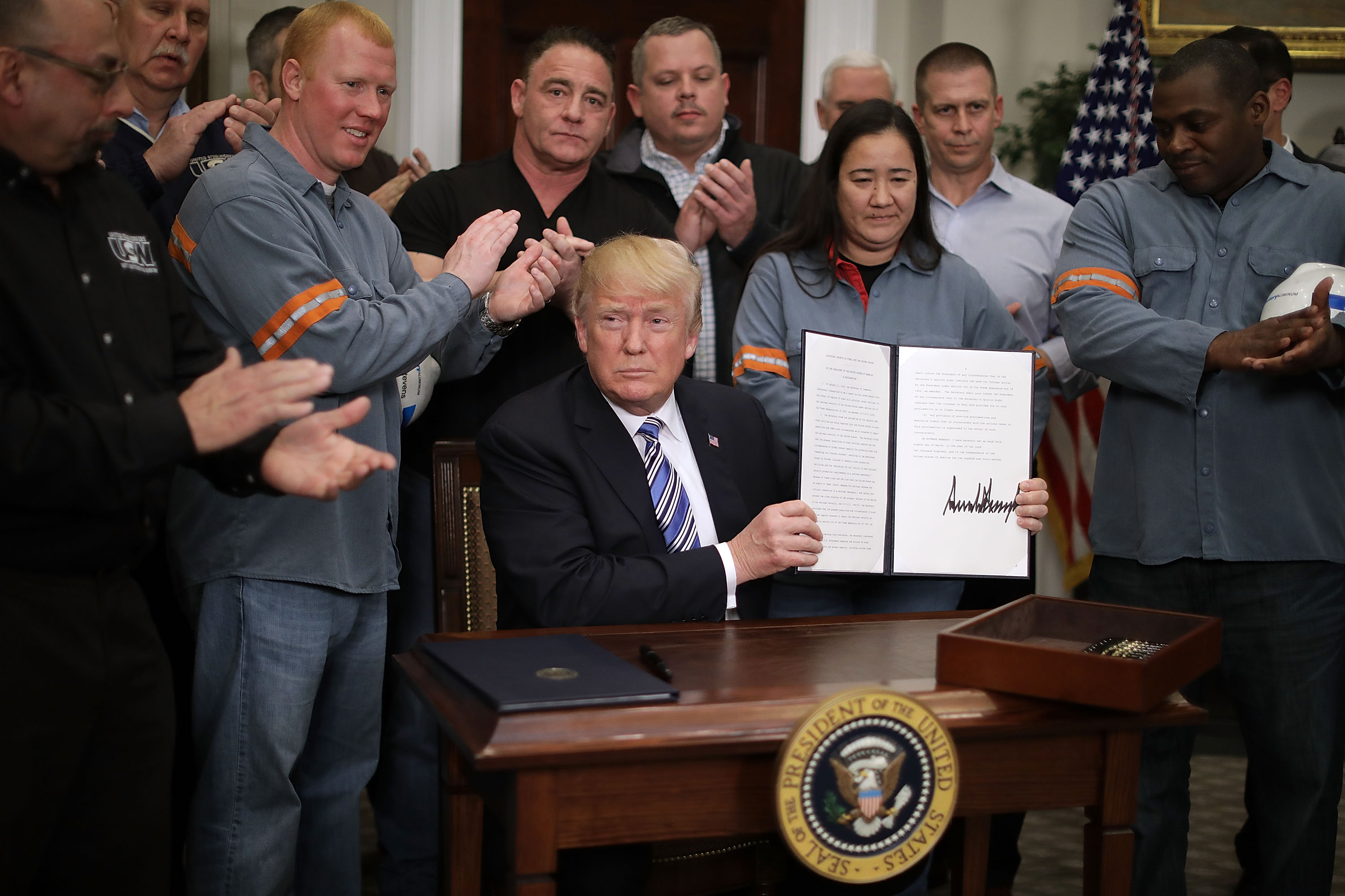 Surrounded by applauding steel and aluminum workers, U.S. President Donald Trump holds up the 'Section 232 Proclamations' on steel imports that he signed in Roosevelt Room the the White House March 8, 2018 in Washington, DC.