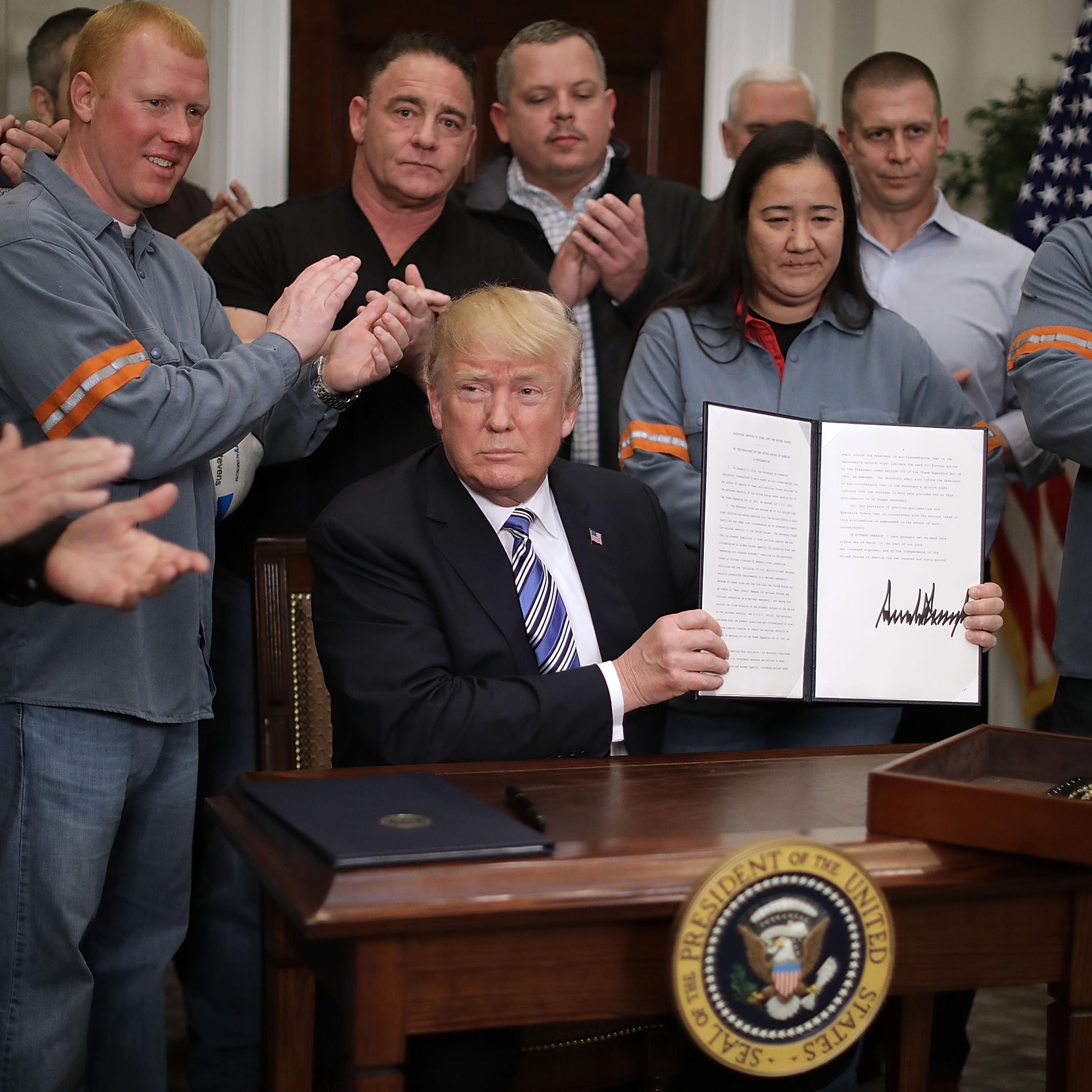 Surrounded by applauding steel and aluminum workers, U.S. President Donald Trump holds up the 'Section 232 Proclamations' on steel imports that he signed in Roosevelt Room the the White House March 8, 2018 in Washington, DC.