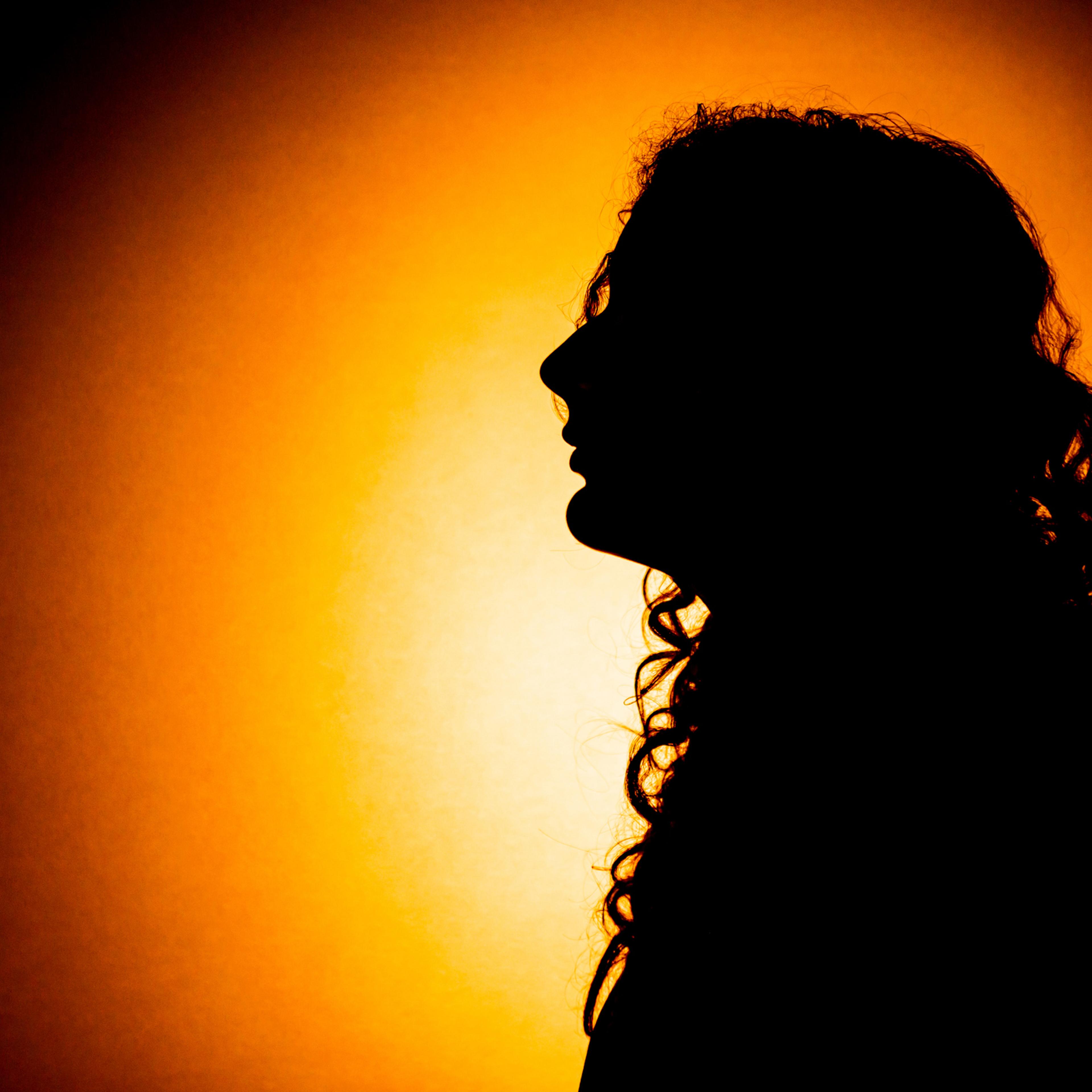 Silhouette of a young woman with long curly hair against an orange background