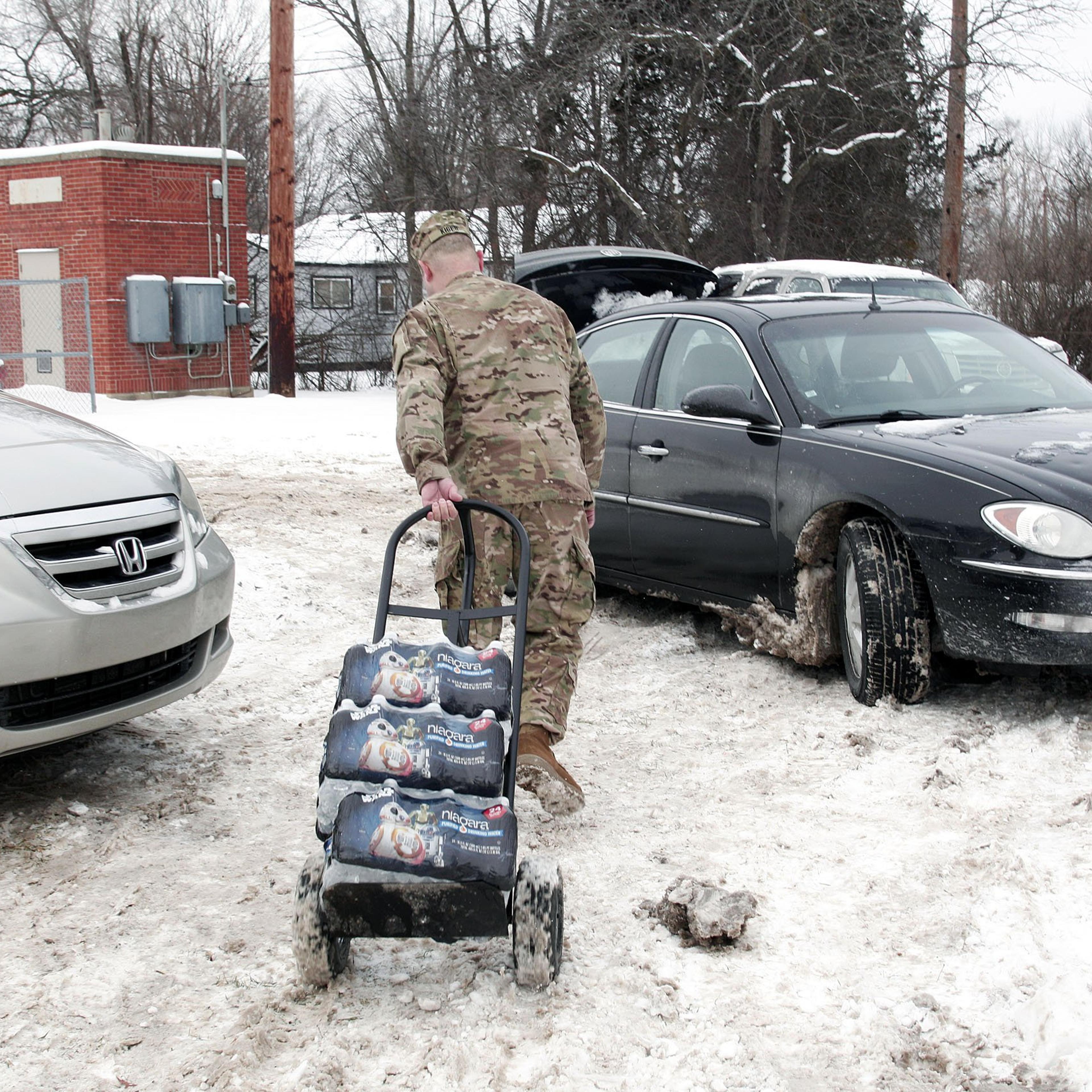 Michigan National Guard Staff Sergeant Steve Kiger of Beaverton, Michigan, helps Christine Brown of Flint, Michigan take bottled water out to her car after she received it at a Flint Fire Station on Jan 13, 2016 in Flint, Michigan.